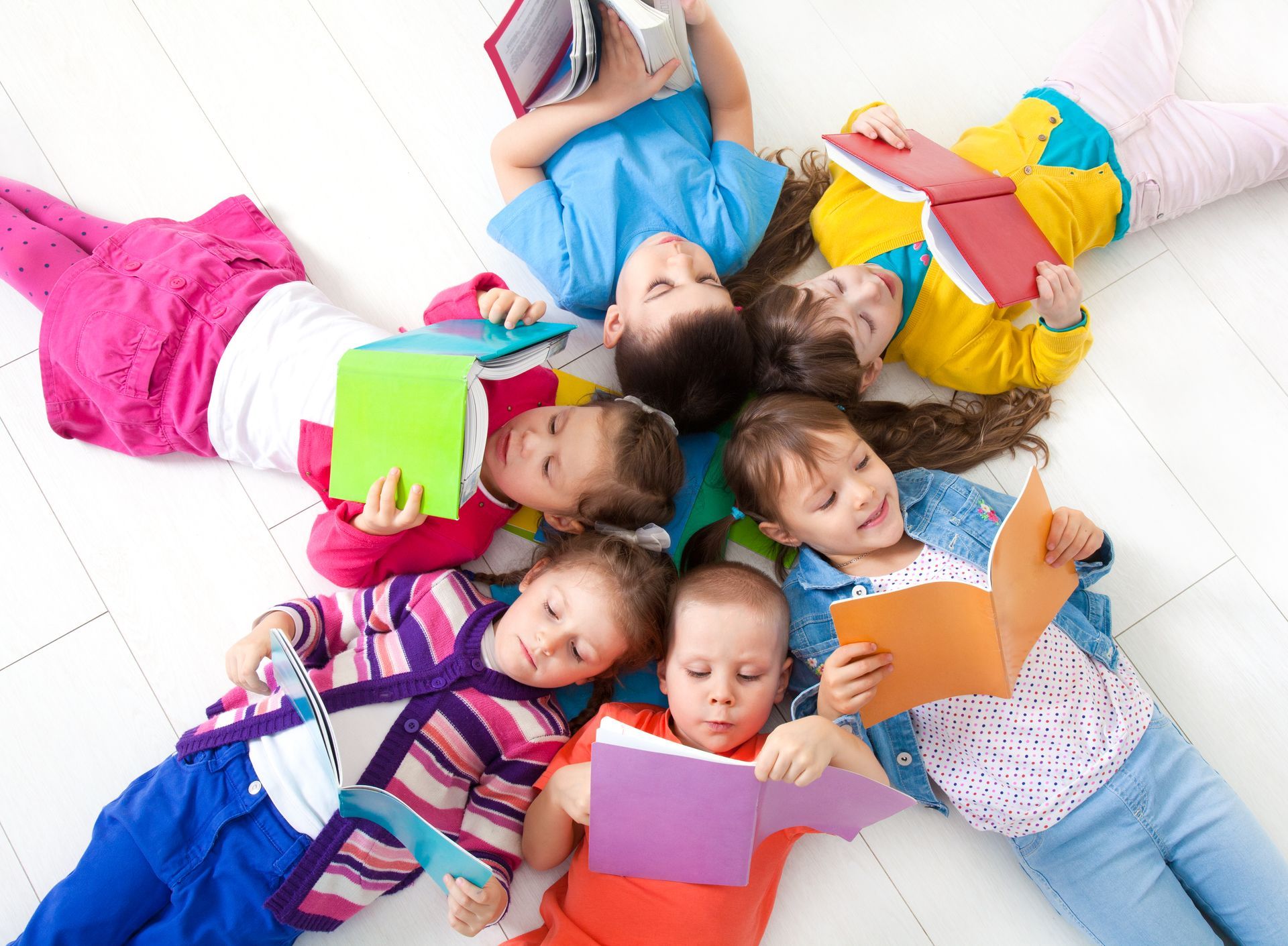 A group of children are laying on the floor reading books.