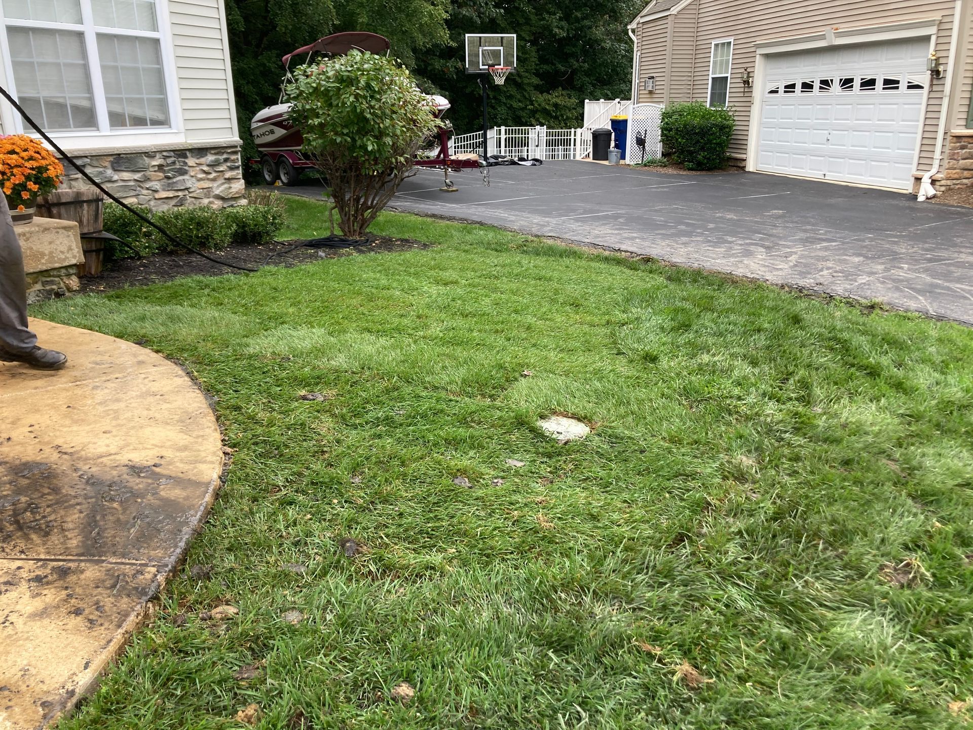 Front lawn with a basketball hoop, driveway, garage, and shrubs beside a house.