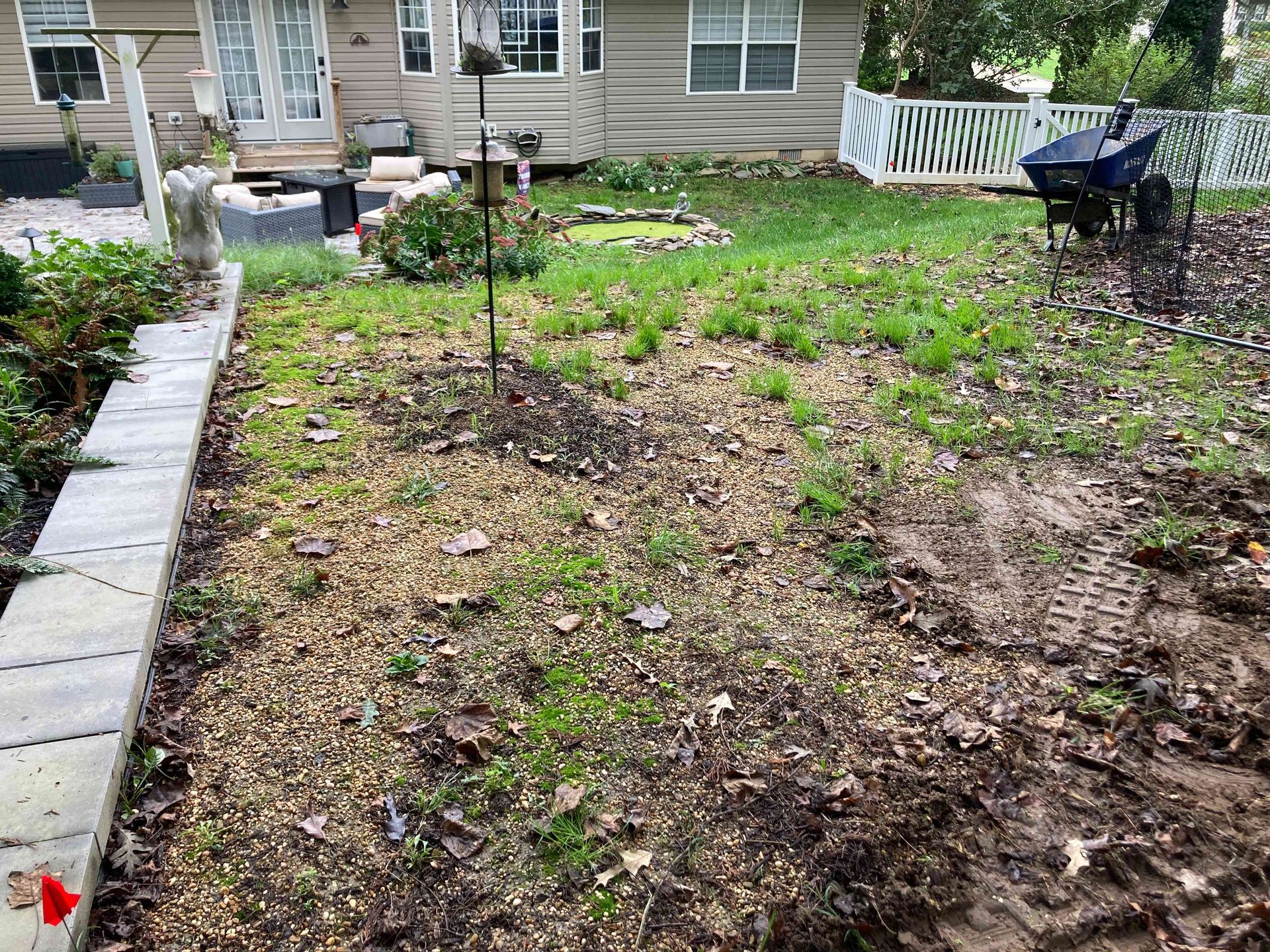 Front yard with sparse grass, flower beds, a stone border, and a patio outside a house