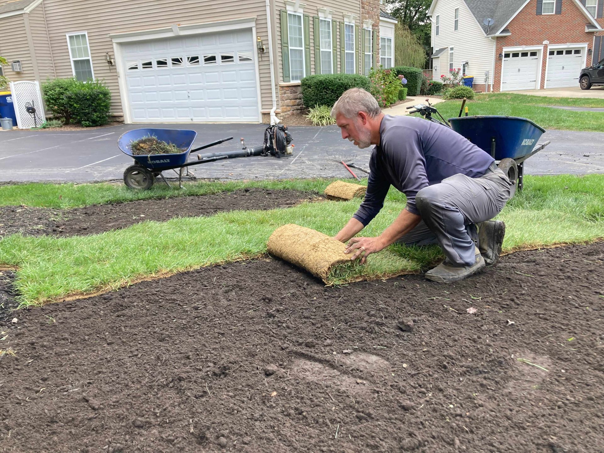 Person rolling sod in a suburban front yard near a driveway and garage
