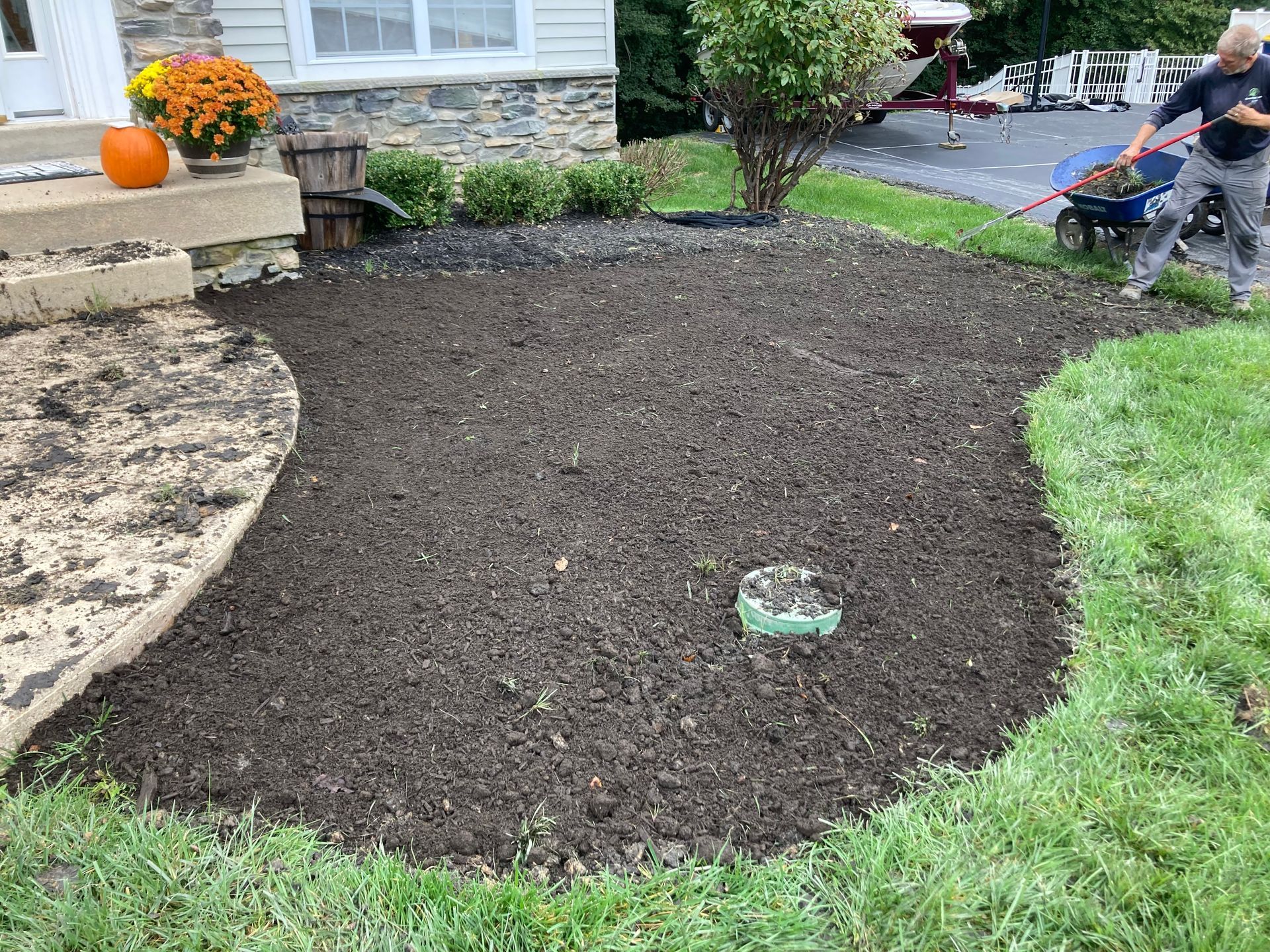 Freshly mulched front yard bed with a pumpkin on the porch and a worker edging the lawn in the background