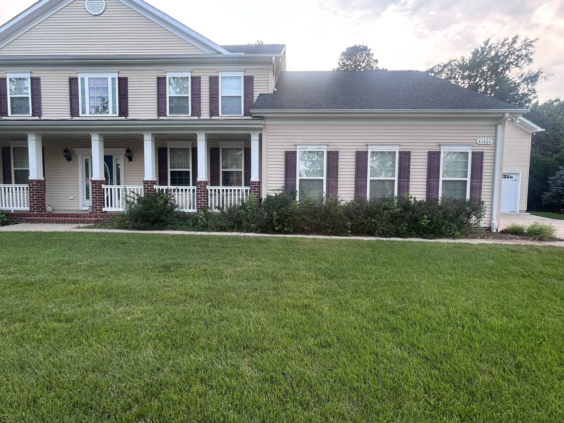 Two-story brick house with white porch, maroon shutters, and a green front lawn