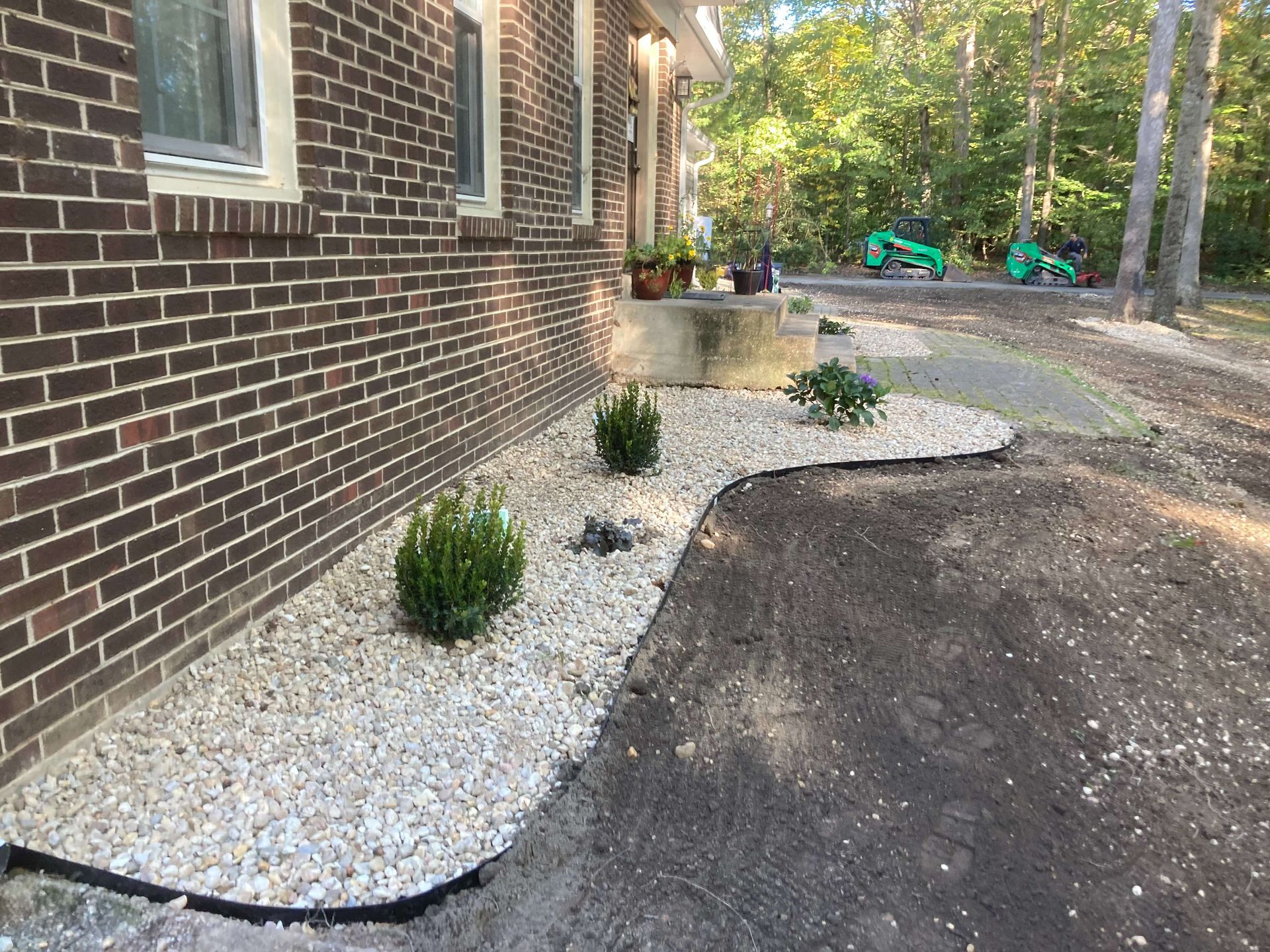 Brick house with new white gravel landscaping and small shrubs beside a dark driveway.