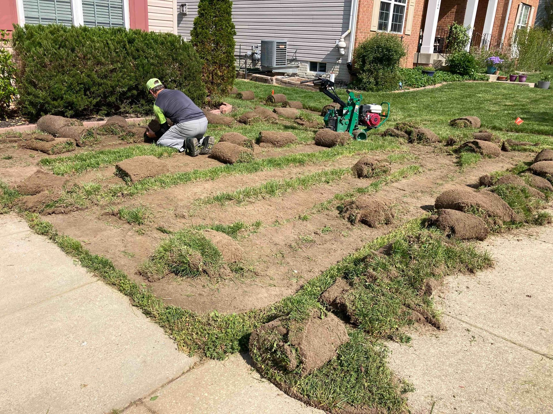 Two workers laying sod in a front yard beside a sidewalk and house.