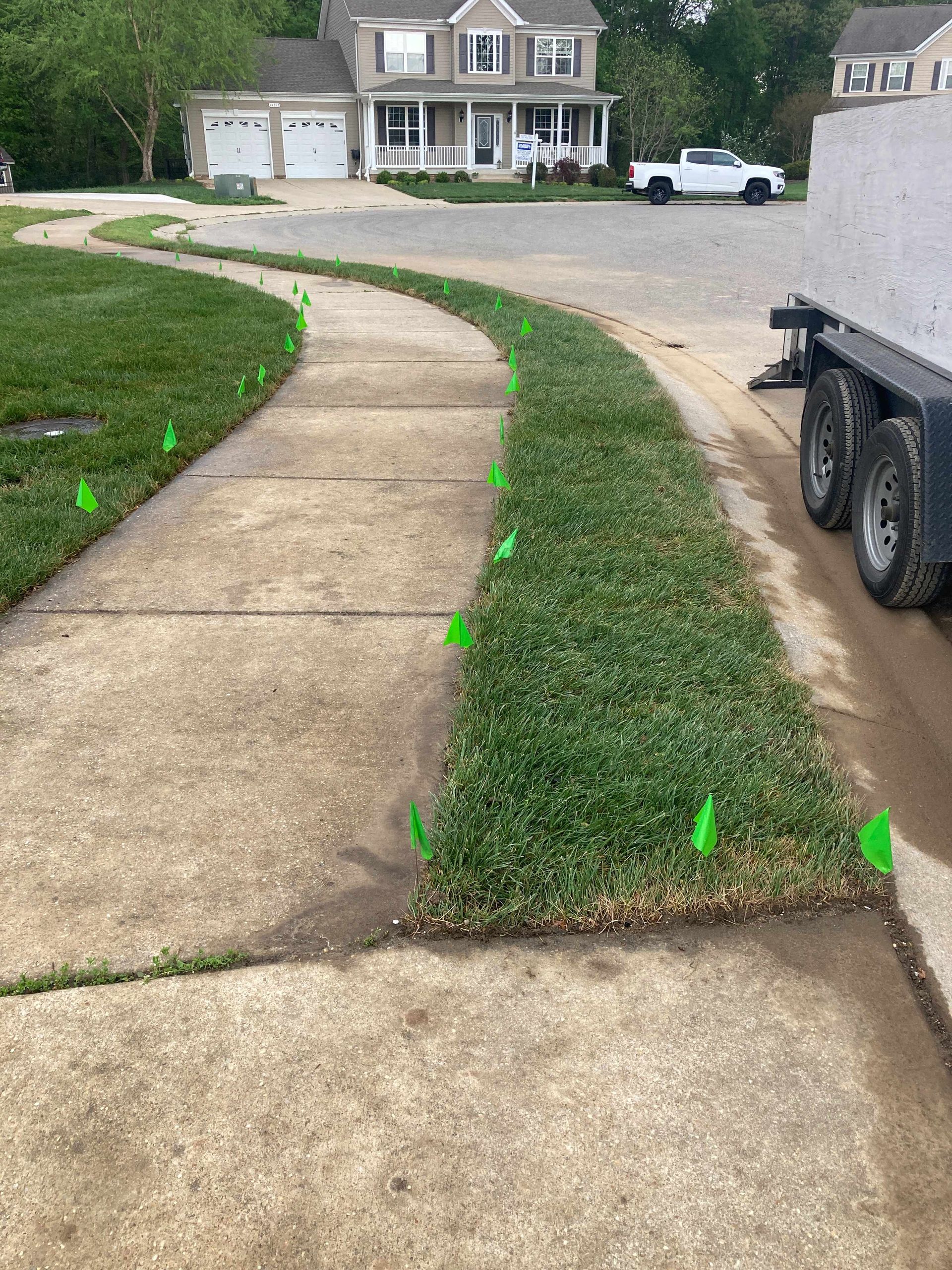 Curved concrete driveway beside a grassy strip marked with green flags, leading to a suburban house.