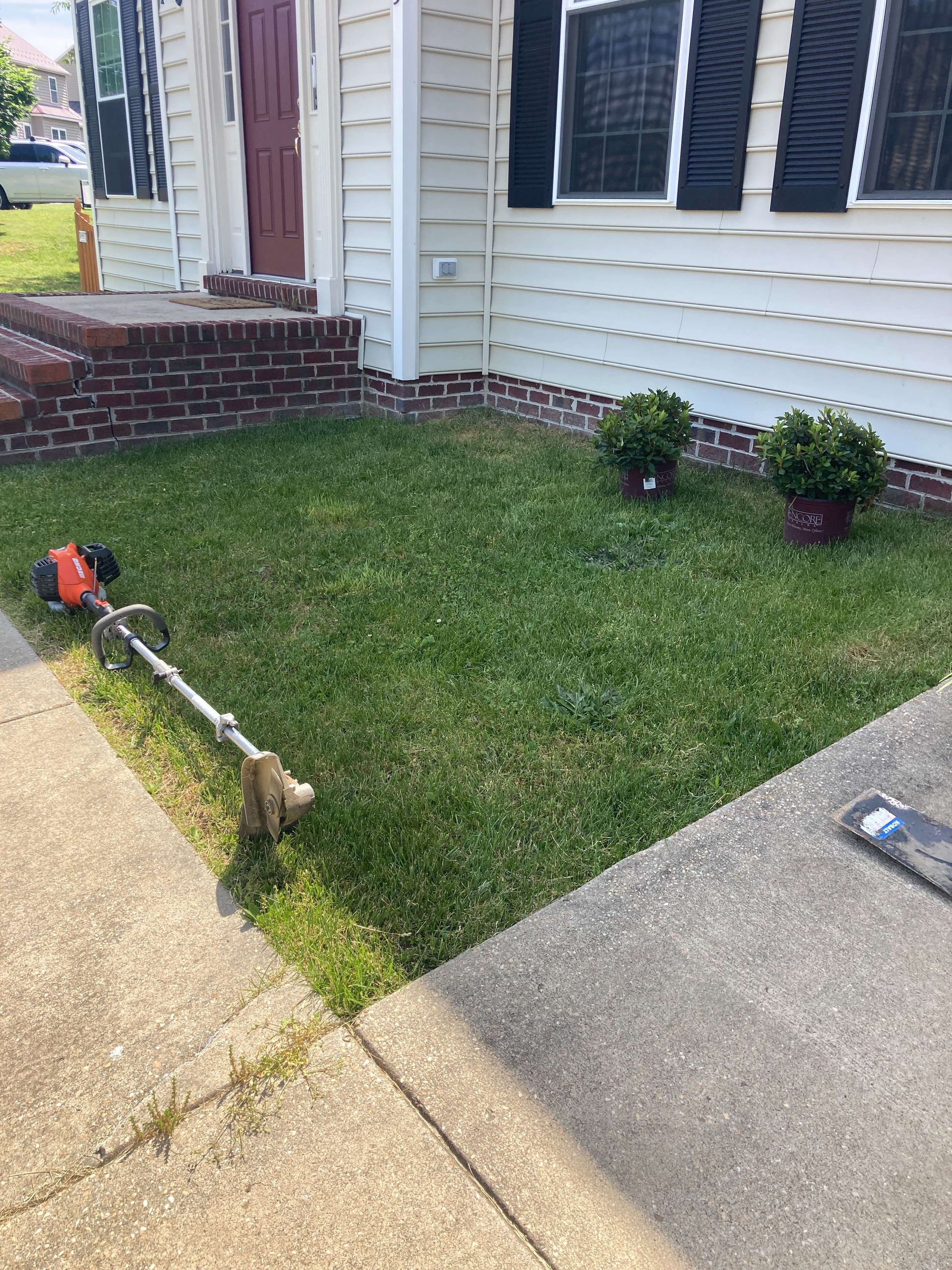 Backyard side yard with house siding, gravel border, grass lawn, utility equipment, and white fence.