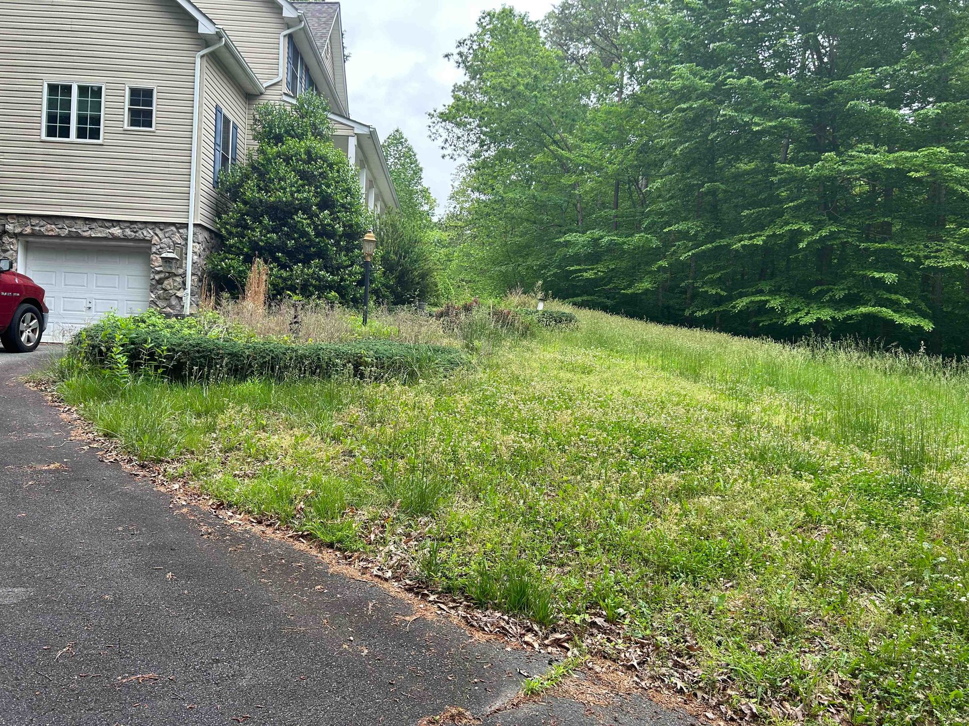 Suburban house beside a sloped grassy yard and driveway with a red car partly visible on the left.