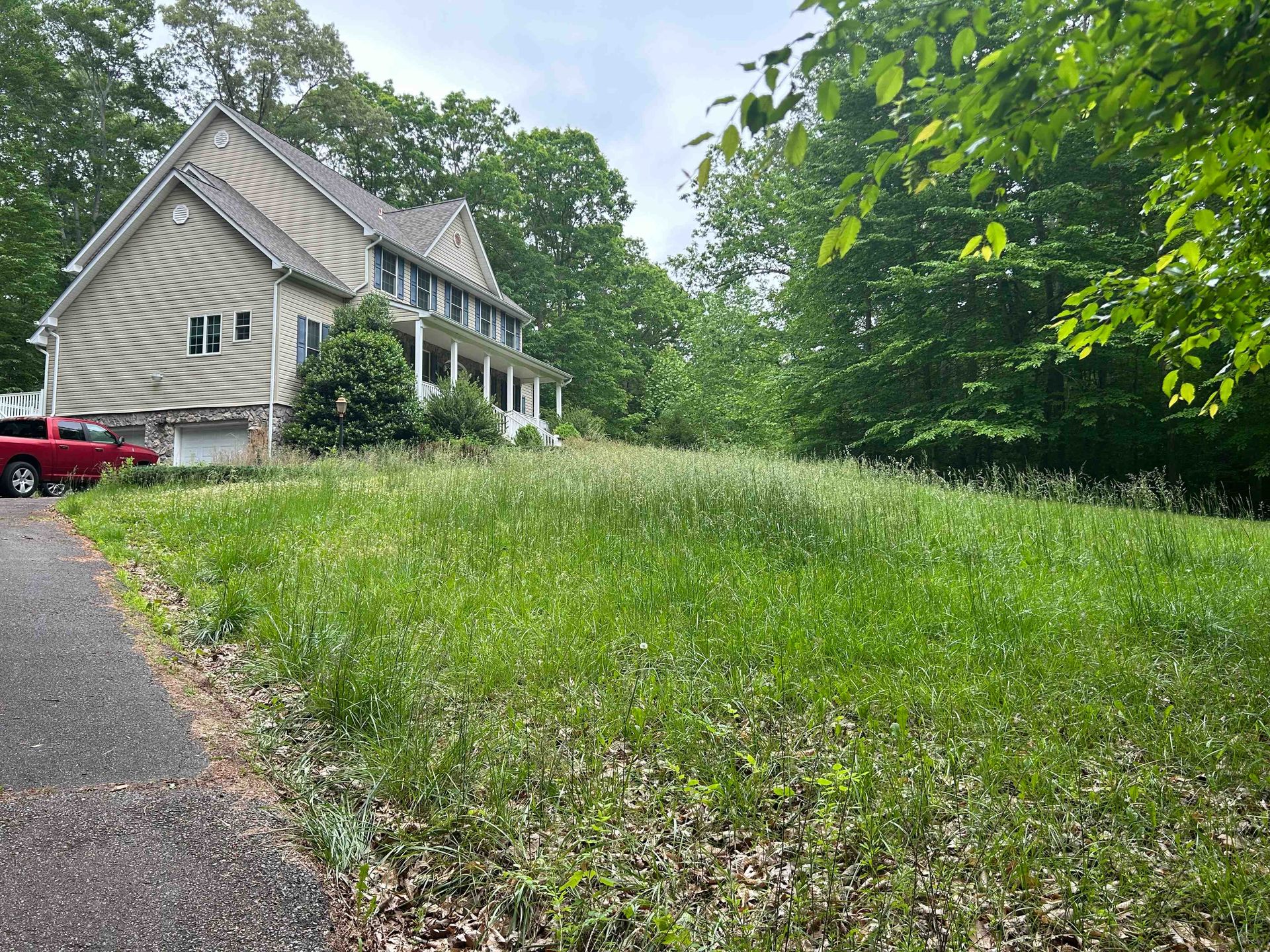 House with a front porch beside a grassy yard and driveway, surrounded by trees.