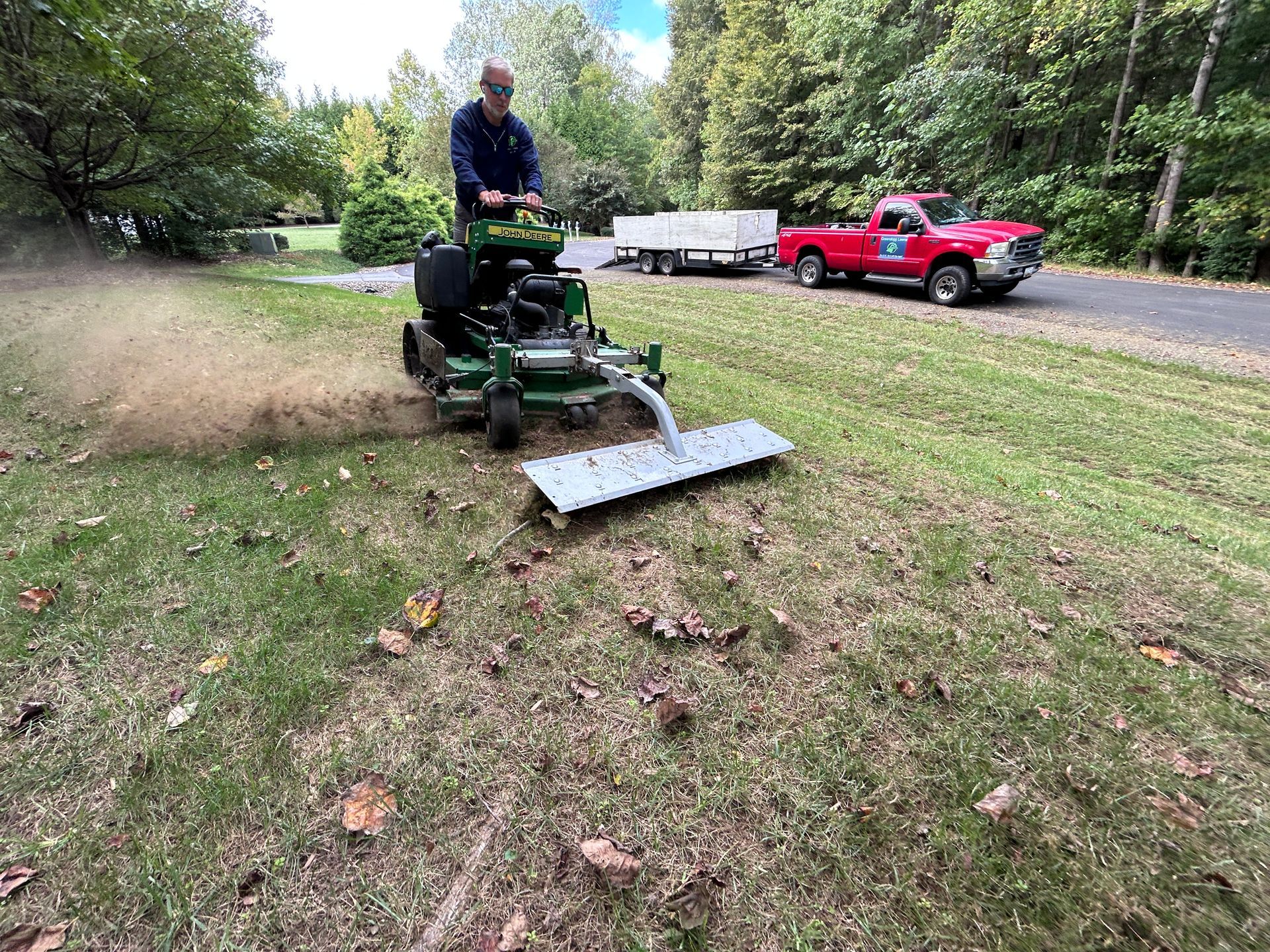 Person mowing grass with a riding mower near a red truck in a yard.