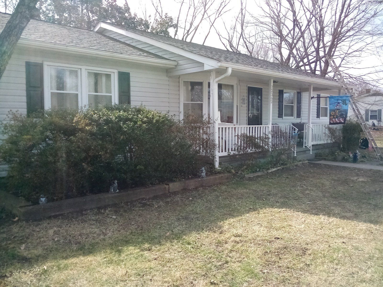 Small white house with a front porch, shrubs, and a grassy yard in daylight
