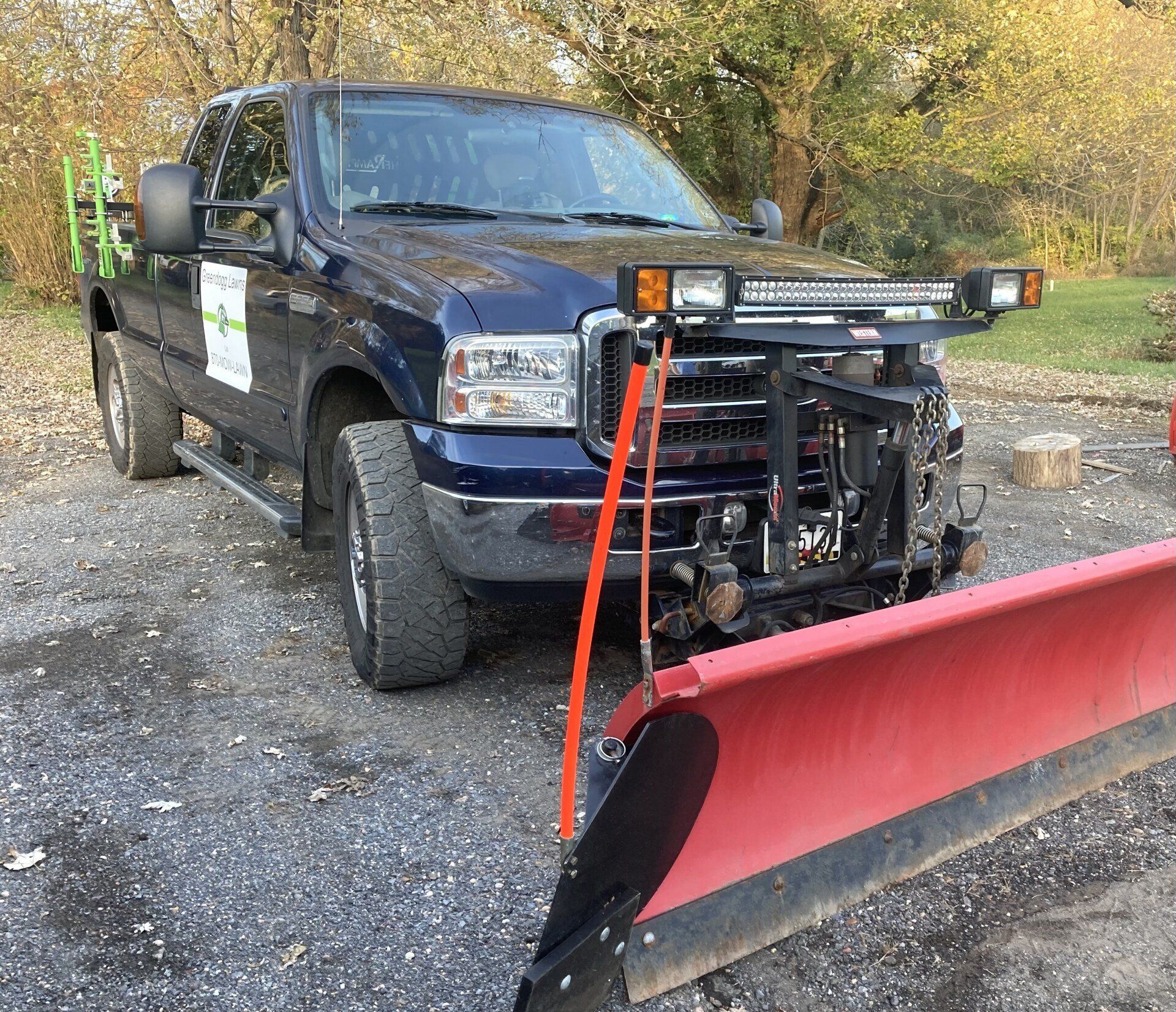 Pickup truck with a front-mounted snowplow parked on a gravel driveway in fall.