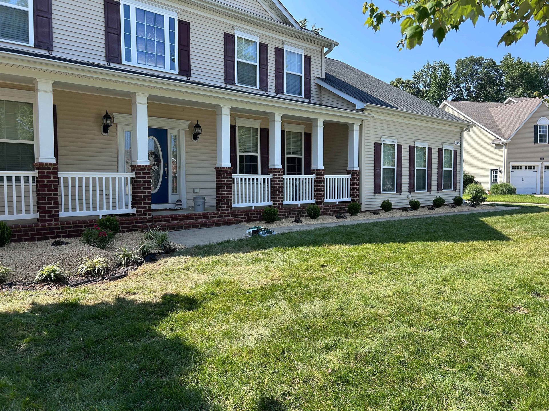 Suburban two-story house with white porch columns, brown shutters, and a green front lawn