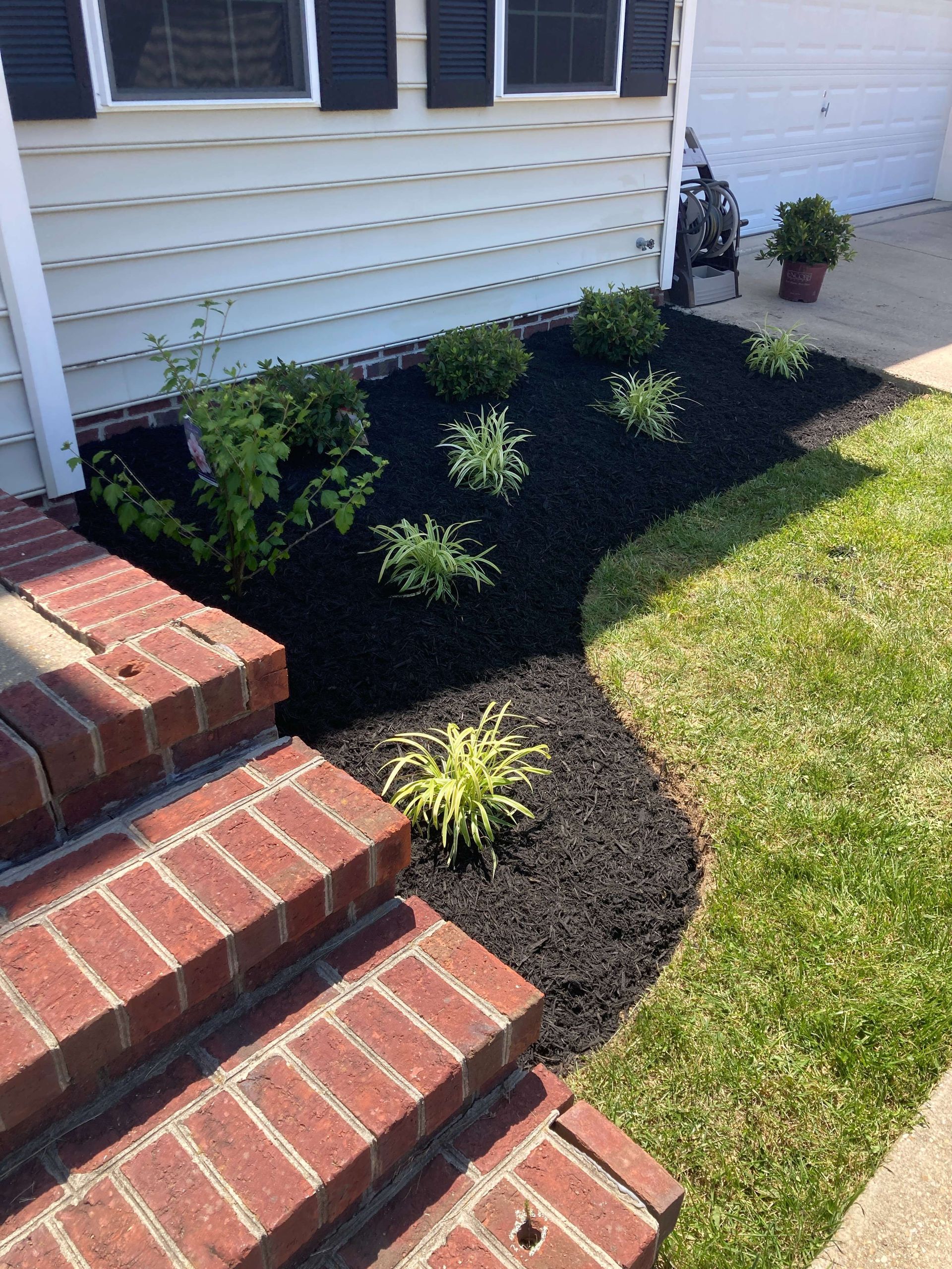 Front steps beside a house with a black mulch flower bed and small green shrubs along a walkway