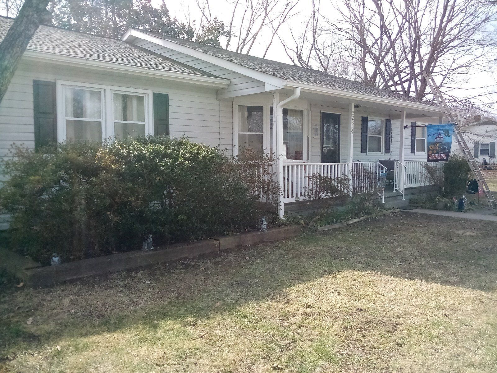 Single-story white house with a front porch, shrubs, and a sunlit lawn