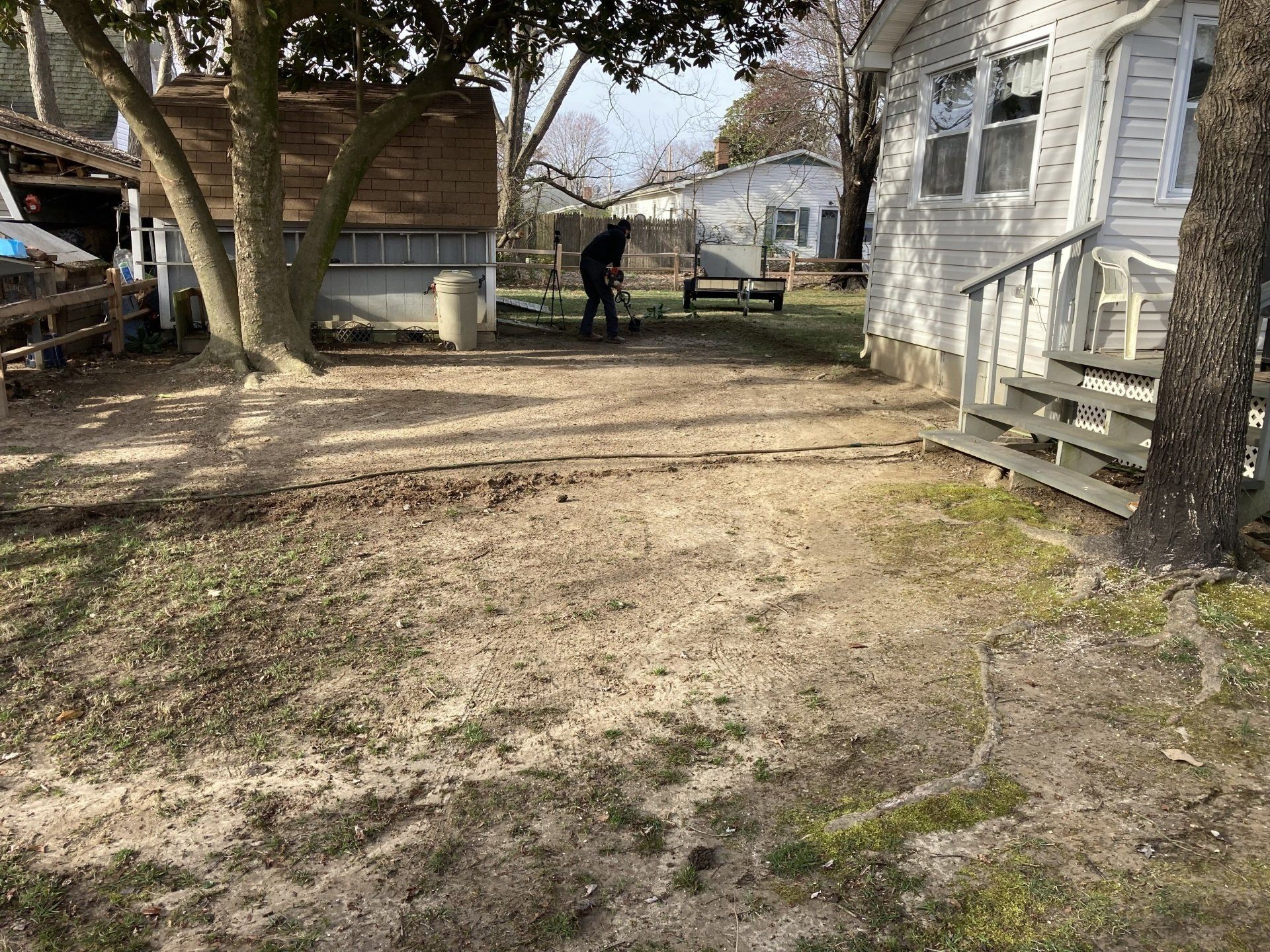 Backyard with bare trees, a wooden shed, and a person working near a fence.