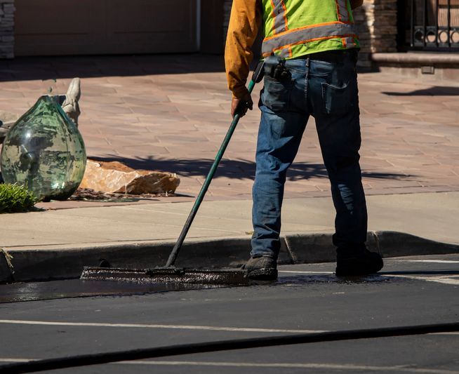 Worker using a sealcoating brush during asphalt resurfacing project