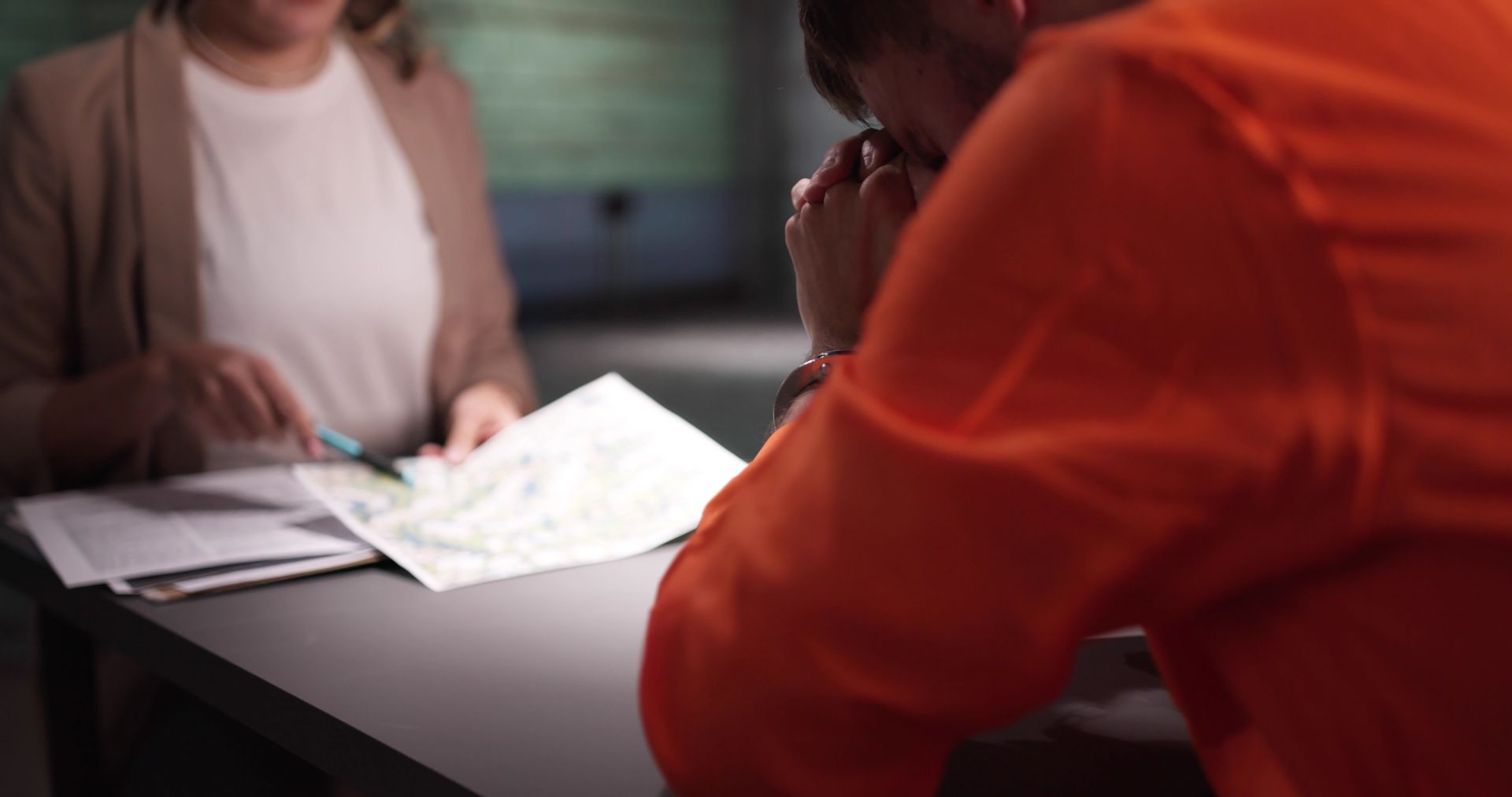 Female criminal lawyer interviewing accused prisoner. Two people discussing a document at a table, with one wearing an orange jacket.
