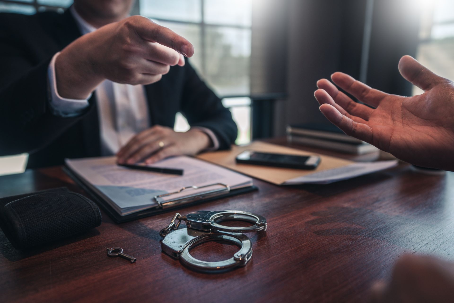 Handcuffs on a table during a legal meeting, with two people gesturing across the desk