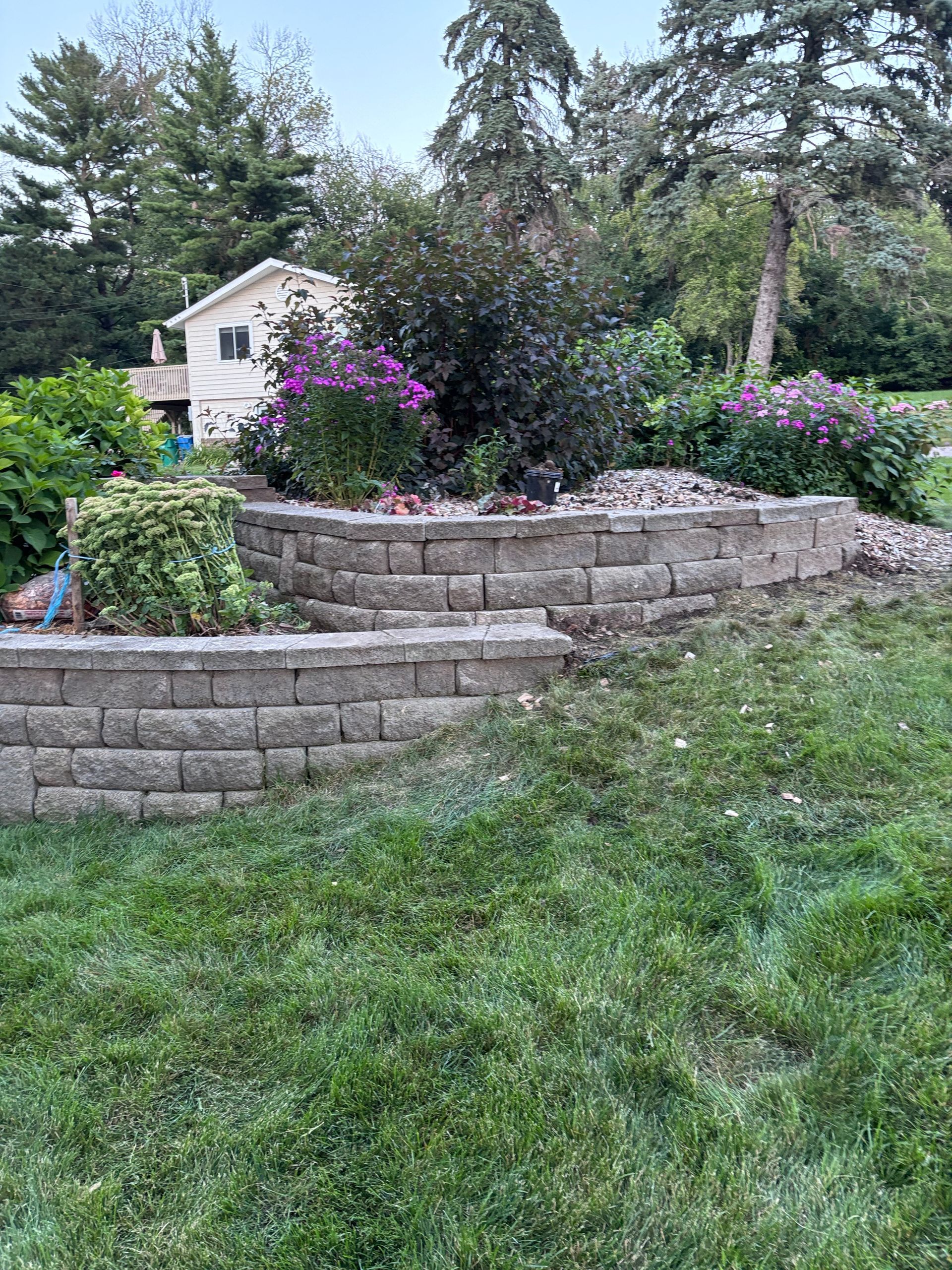 Stone retaining wall with flower beds, house in the background.