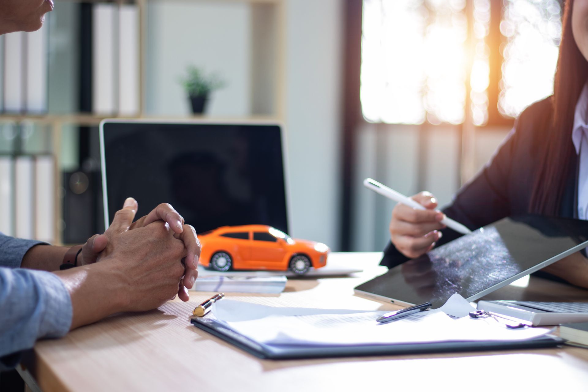 Two people in a meeting with a laptop, papers, and a toy orange car on the table Two people in a meeting with a laptop, papers, and a toy orange car on the table