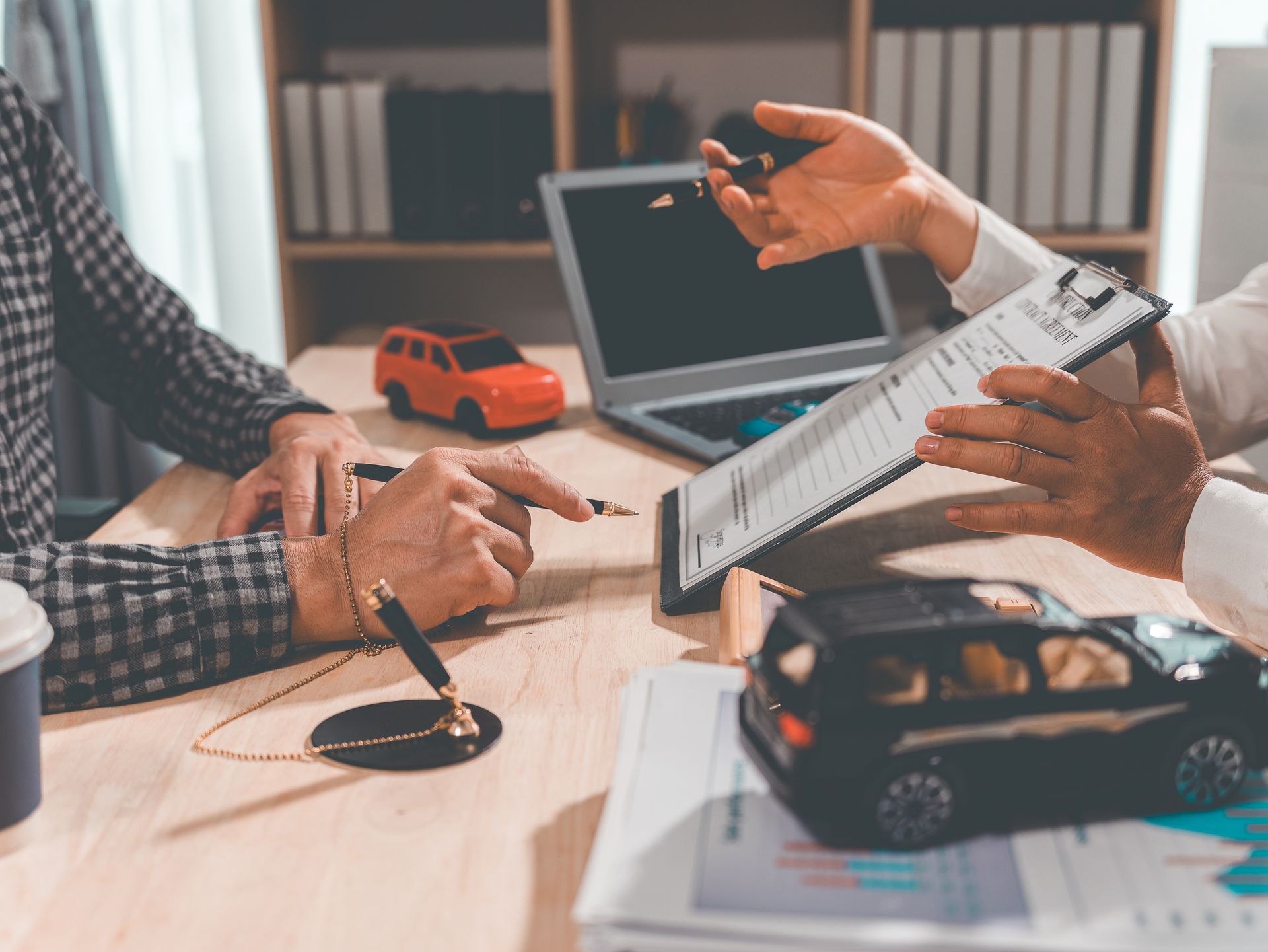 Two people reviewing documents at a desk with a laptop, toy car, and glasses in an office meeting Two people reviewing documents at a desk with a laptop, toy car, and glasses in an office meeting