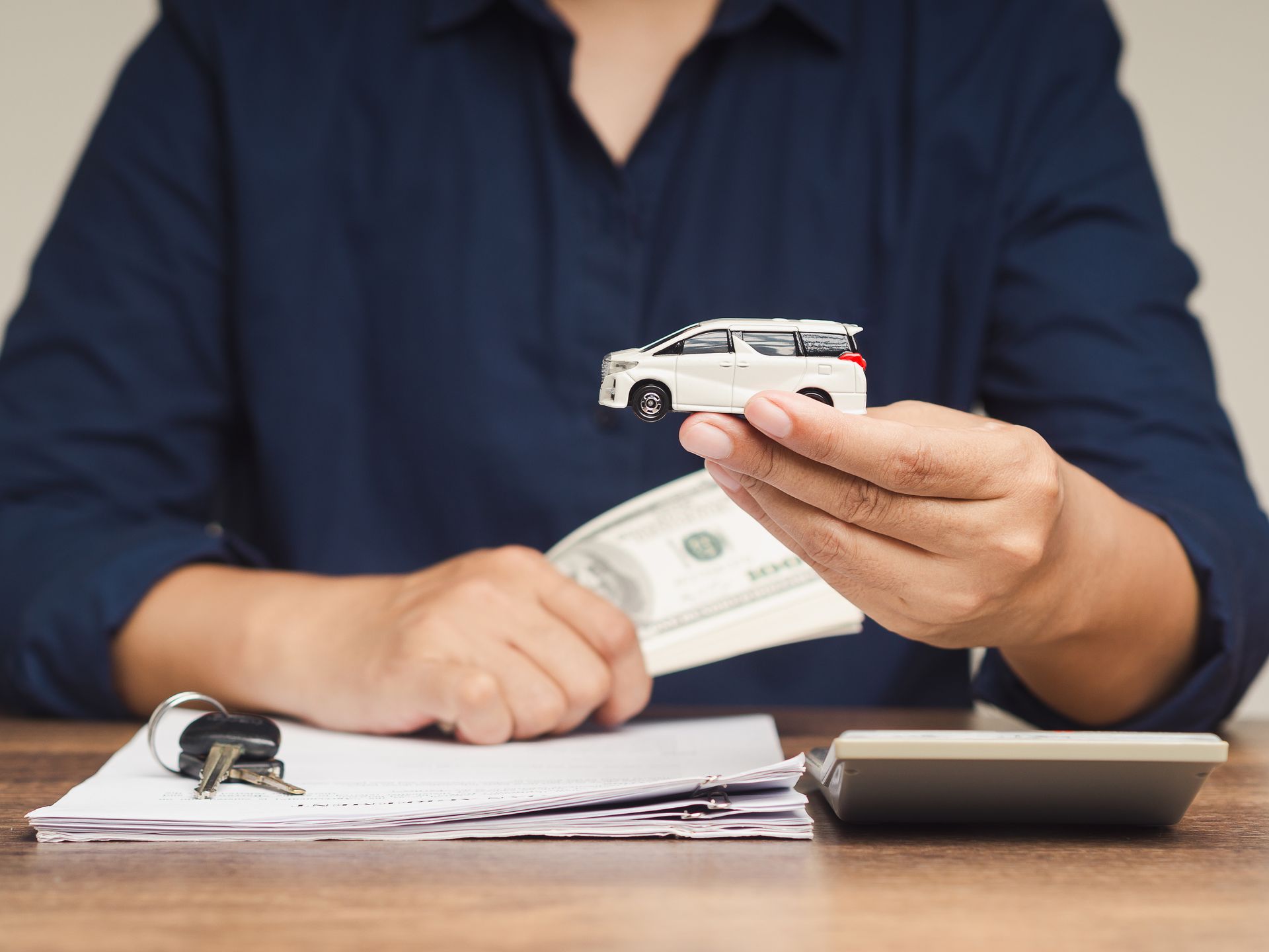 Person counts cash and holds a credit card over paperwork beside a calculator at a desk. Person counts cash and holds a credit card over paperwork beside a calculator at a desk.