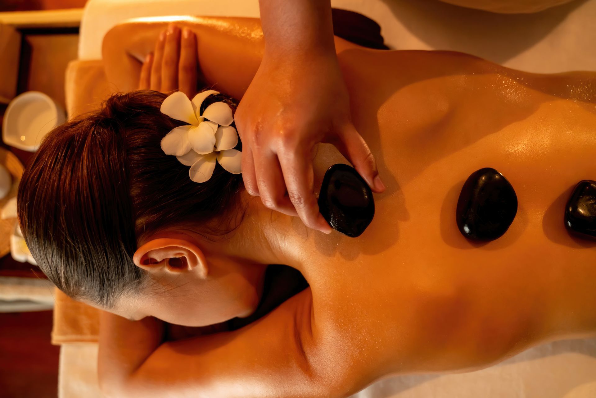 A woman is laying on a massage table with rocks on her back.