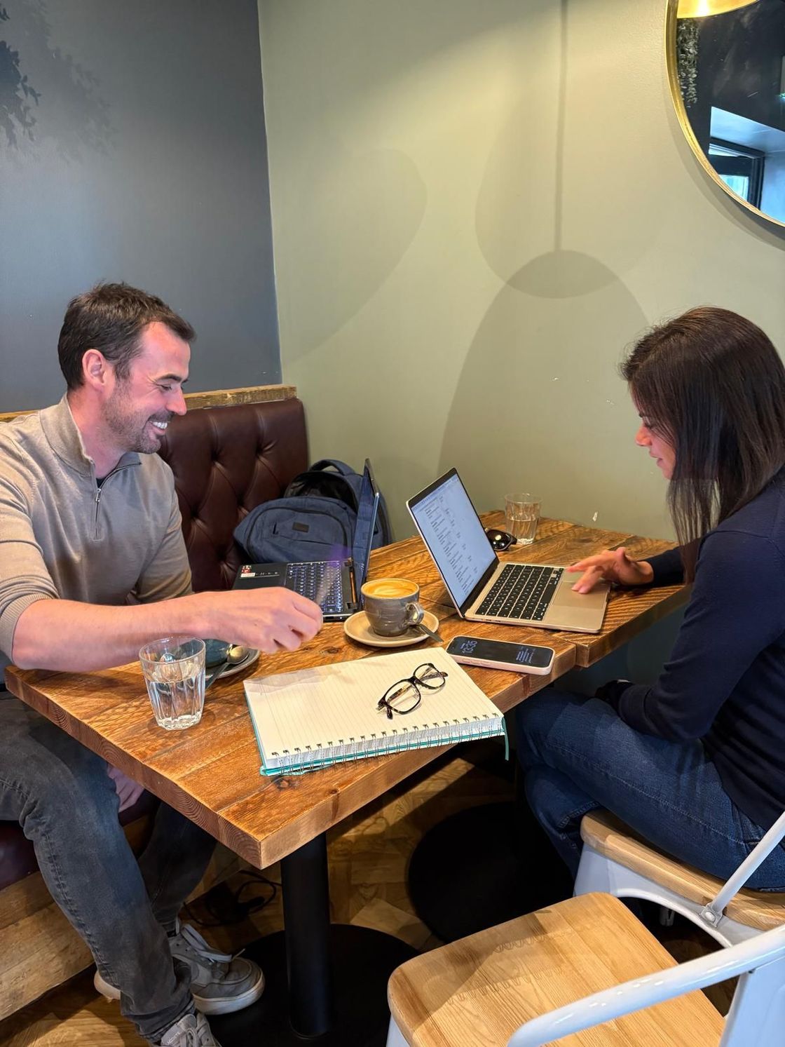 Two people working on laptops at a café table with notebooks and drinks