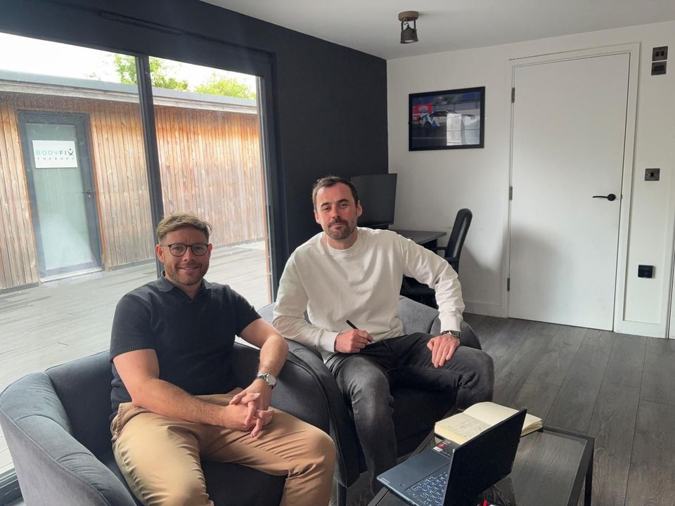 Two people sitting on a couch in a modern living room with a wall-mounted TV and a white door.