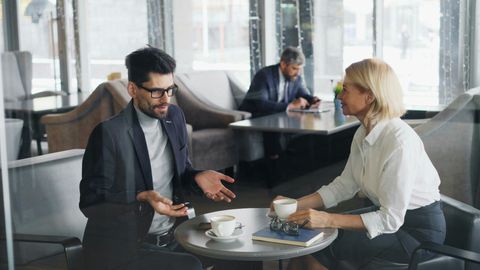 Two people talking over coffee at a table in a bright office lounge
