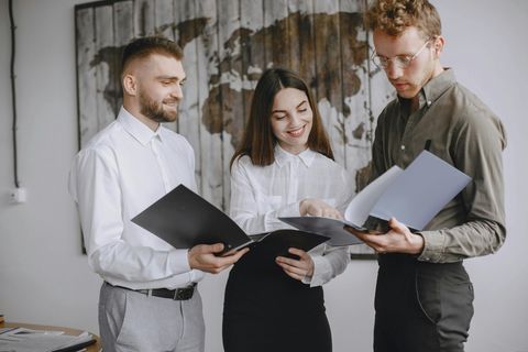 Three people standing together, reviewing documents in a bright office setting.