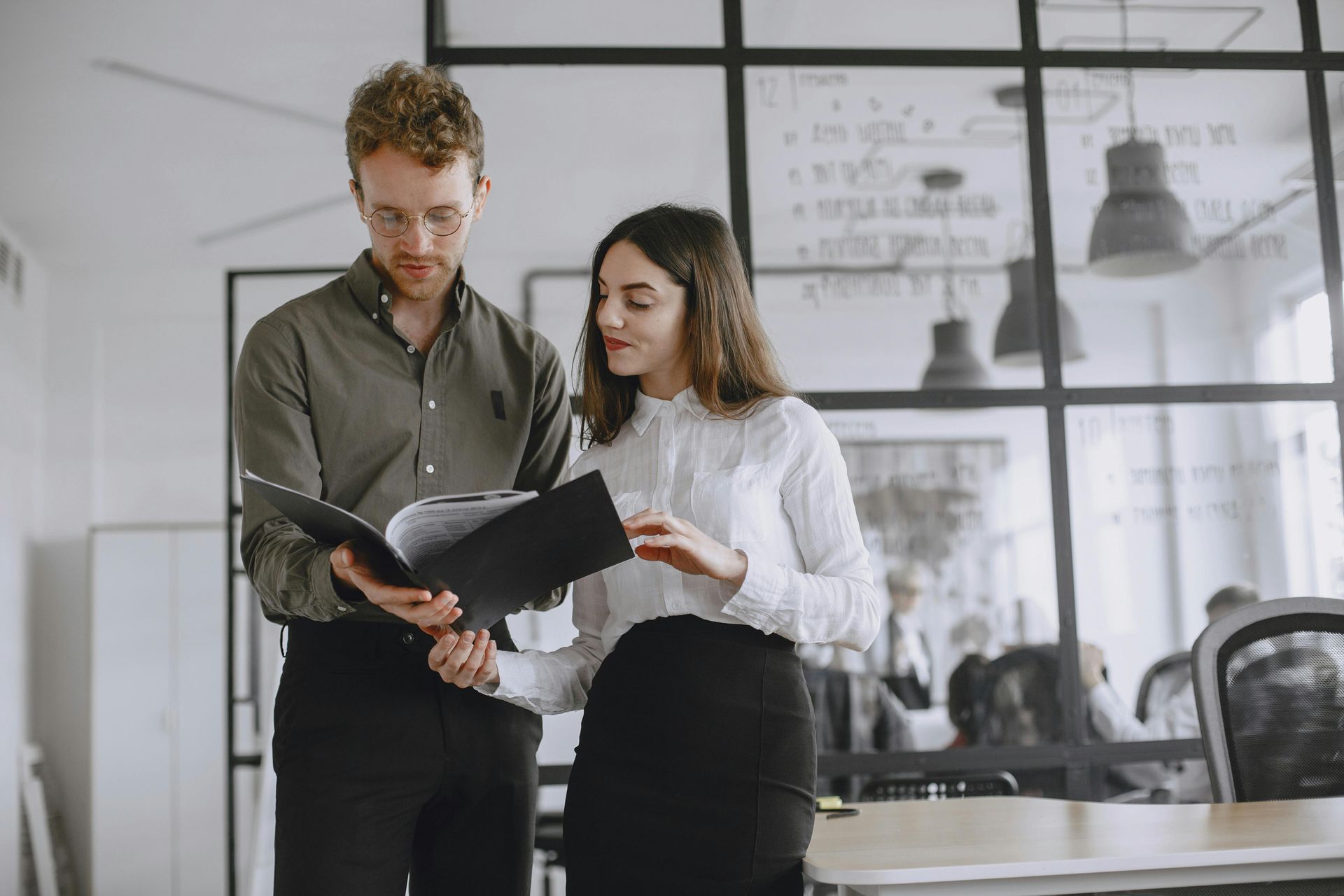 Two coworkers reviewing documents in a modern office with glass walls