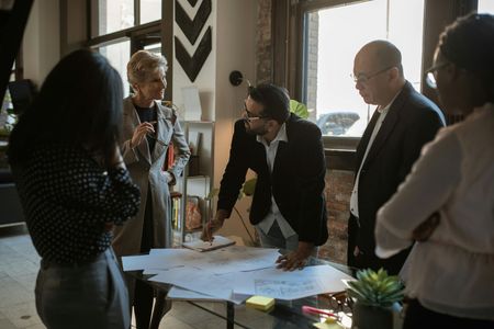 Five colleagues gathered around a table reviewing papers and discussing plans in a bright office.