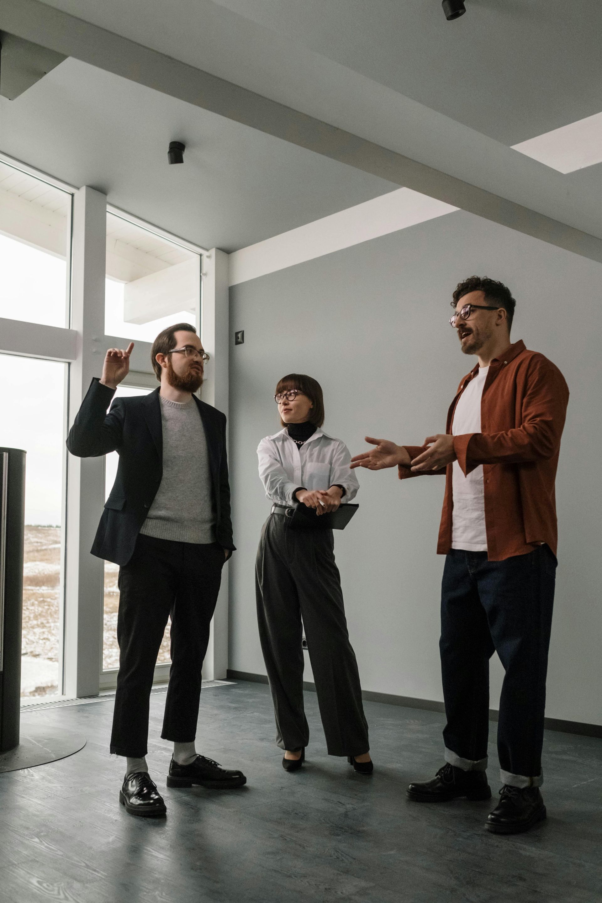 Three people talking in a bright office hallway, one gesturing while the others listen.