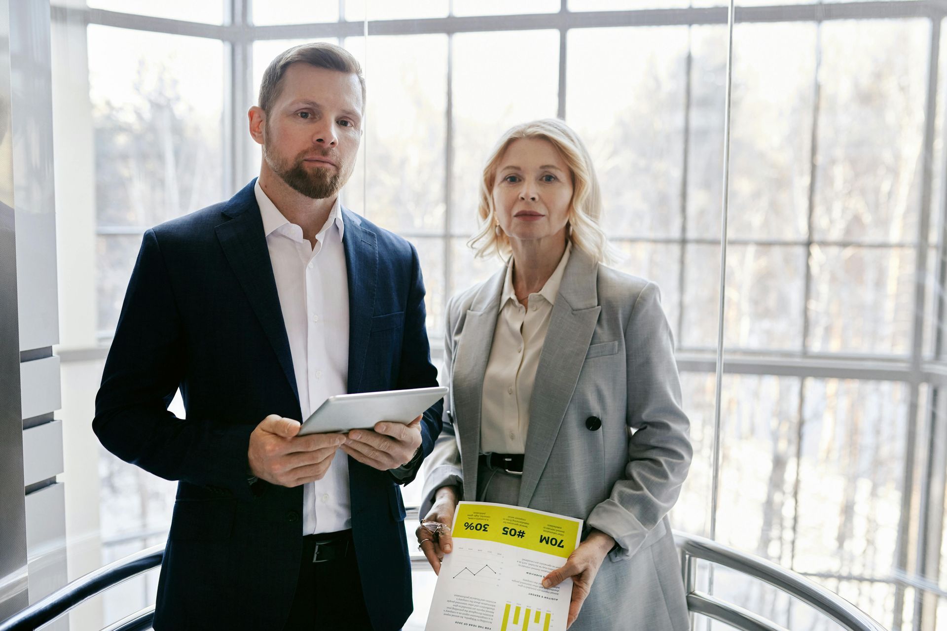 Two professionals holding documents in a bright office with large windows
