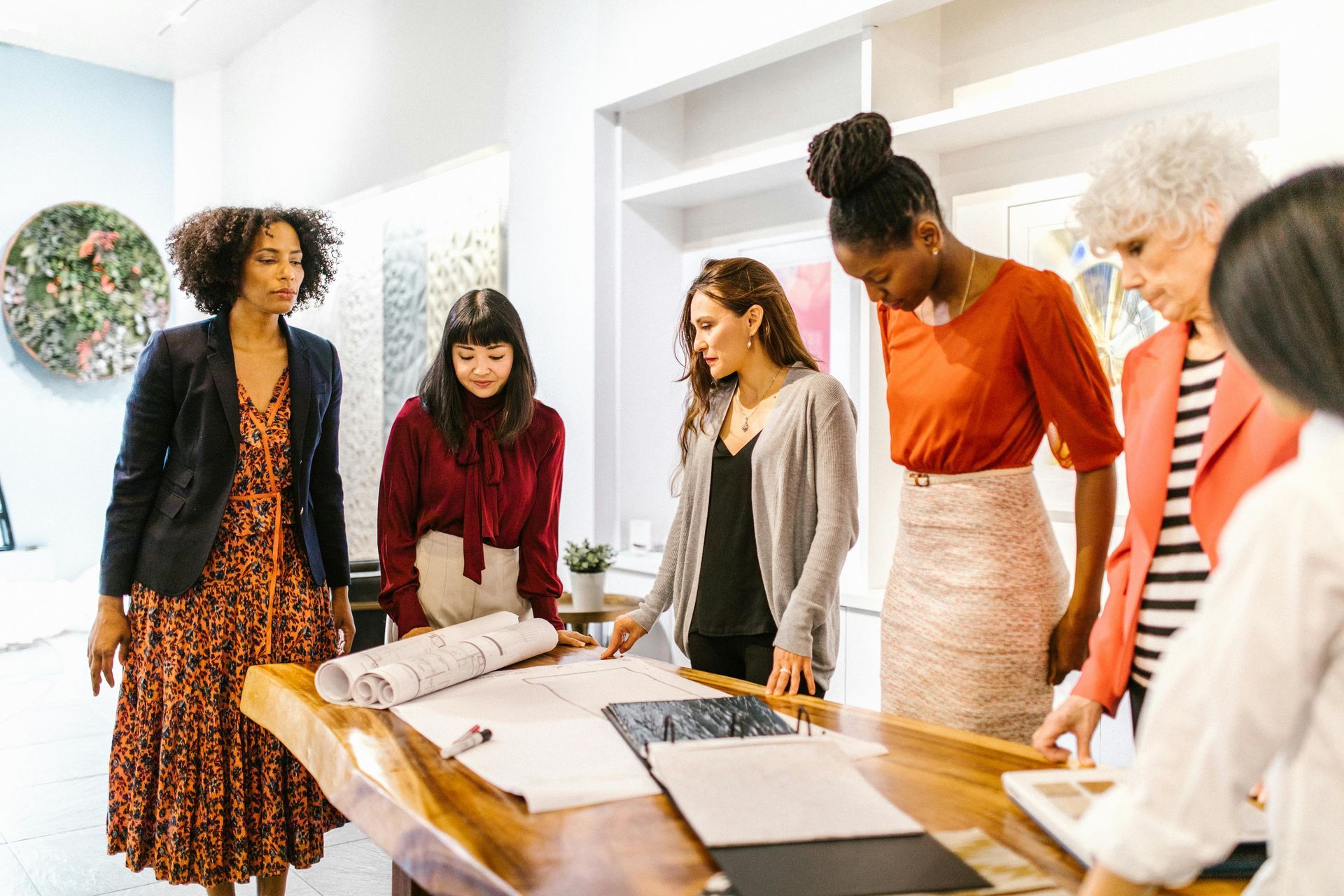 Five people standing around a table reviewing large papers in a bright office