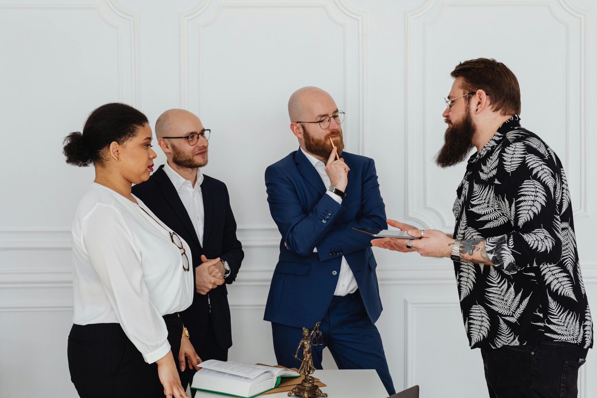 Four coworkers in suits and blazers talking in an office with a white wall backdrop