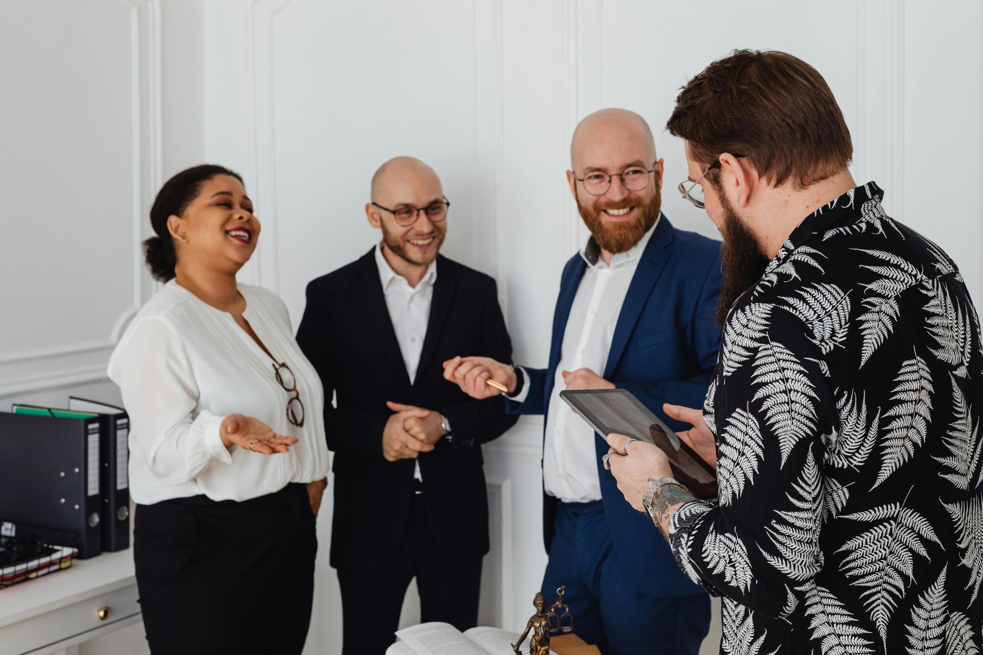 Four coworkers smiling and talking in a bright office while one holds a tablet
