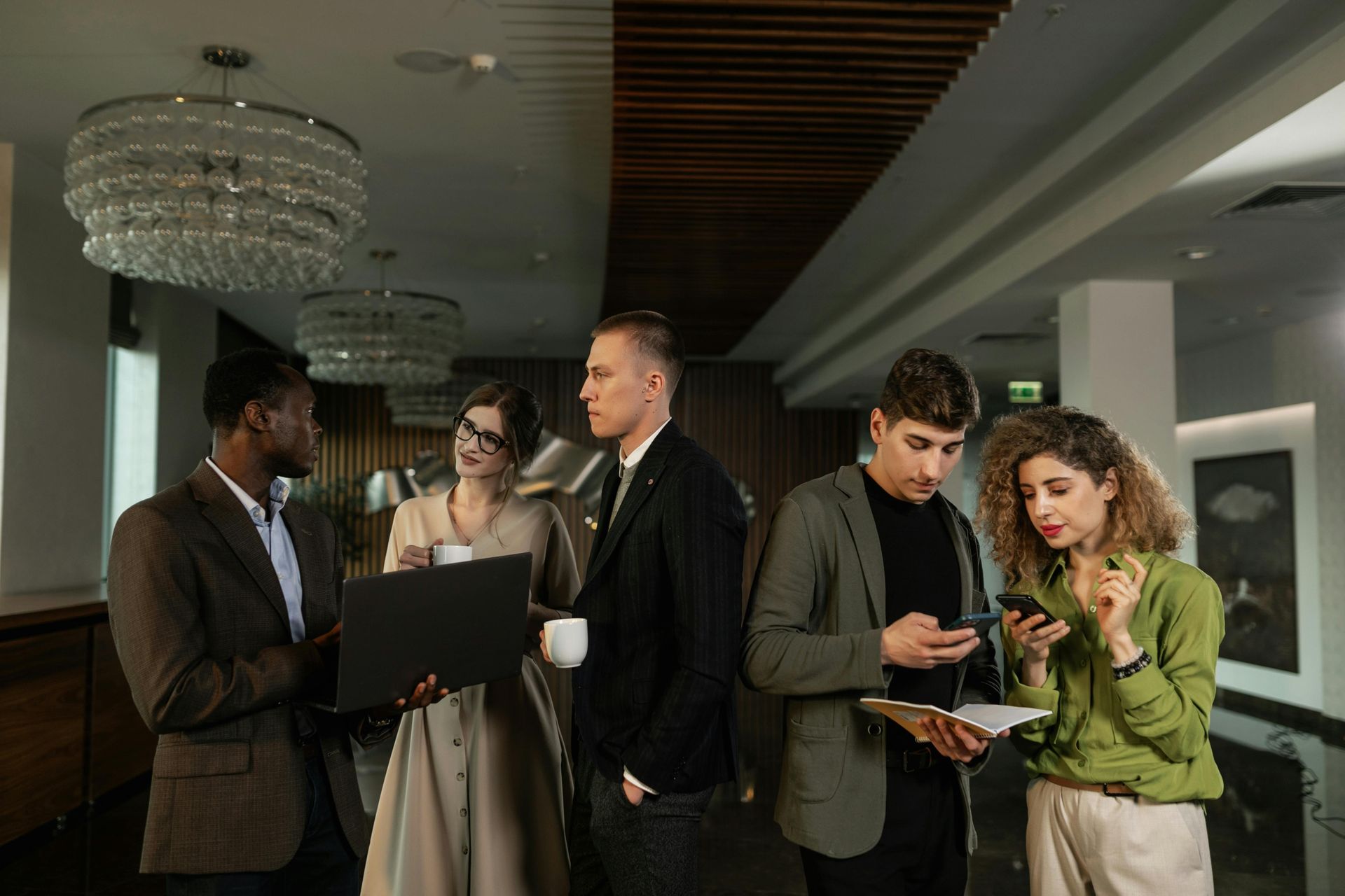 Five people in formal attire discussing documents in a modern lobby with chandeliers
