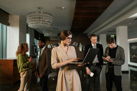People networking in a modern hotel lobby, with one woman holding a tablet in the foreground