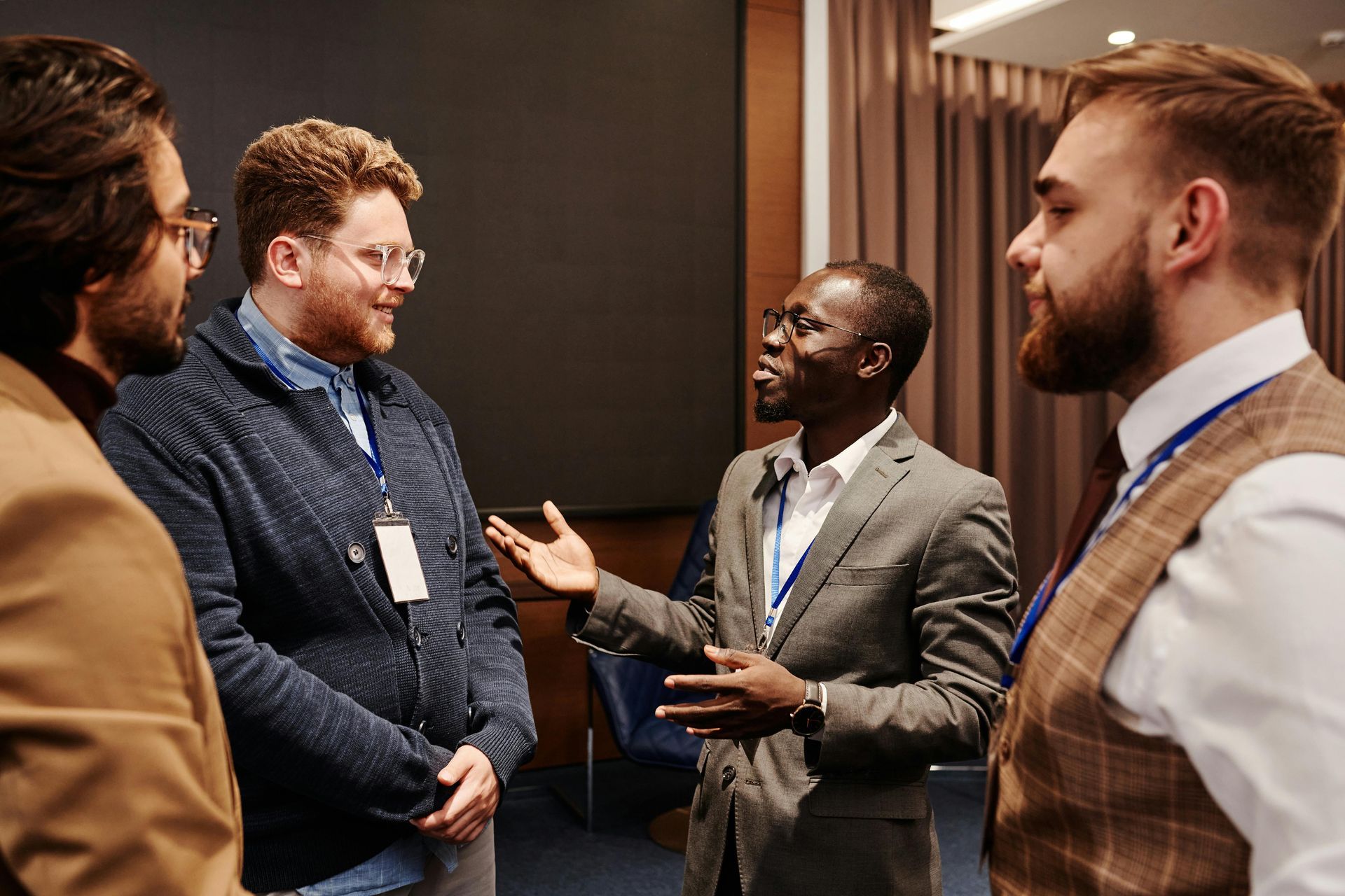 Four people networking at an indoor event, chatting and smiling in business attire.