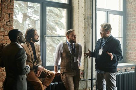Four people talking by large windows in a bright industrial-style room