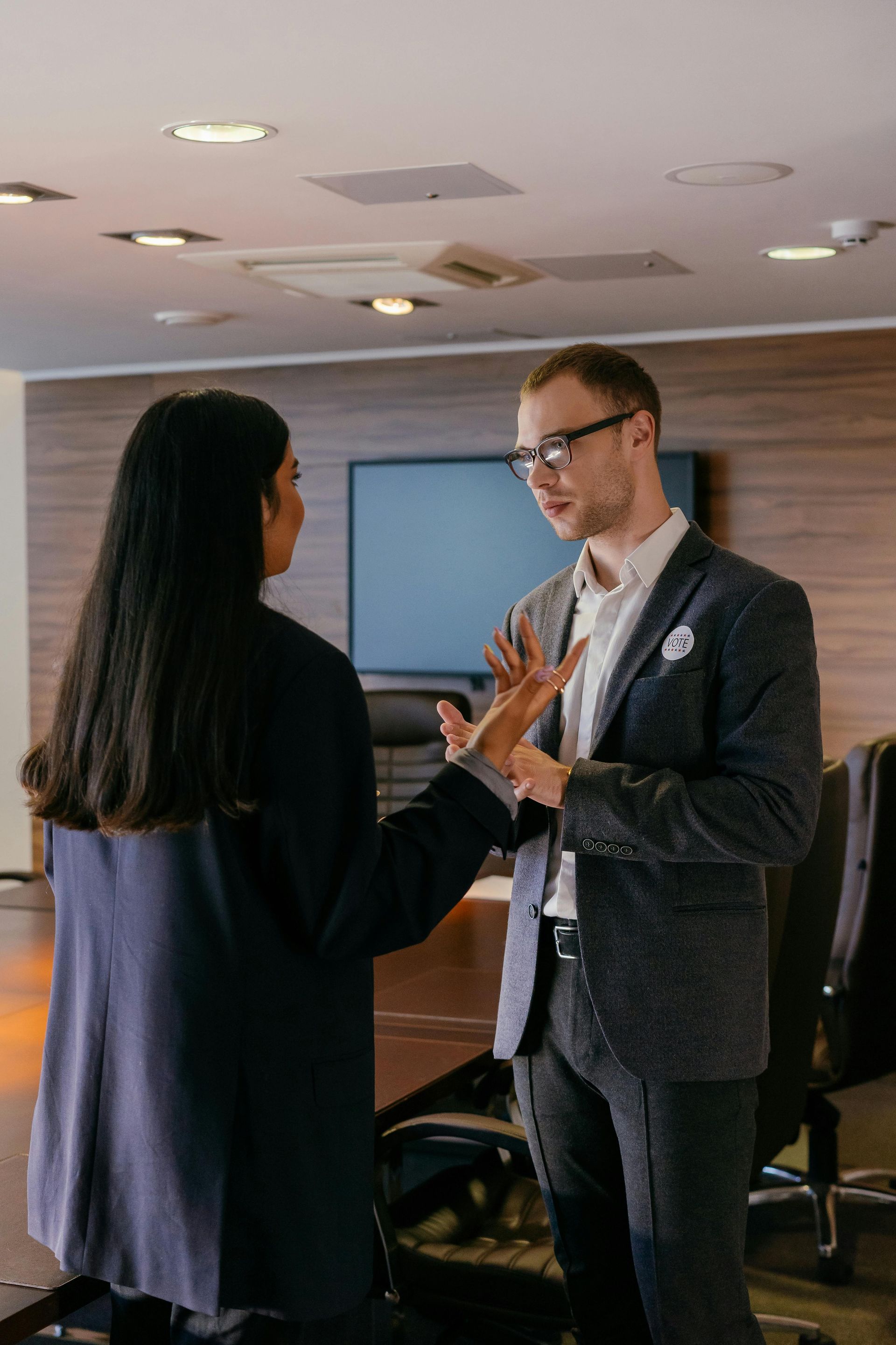 Two coworkers talking in a conference room, gesturing during a business meeting.