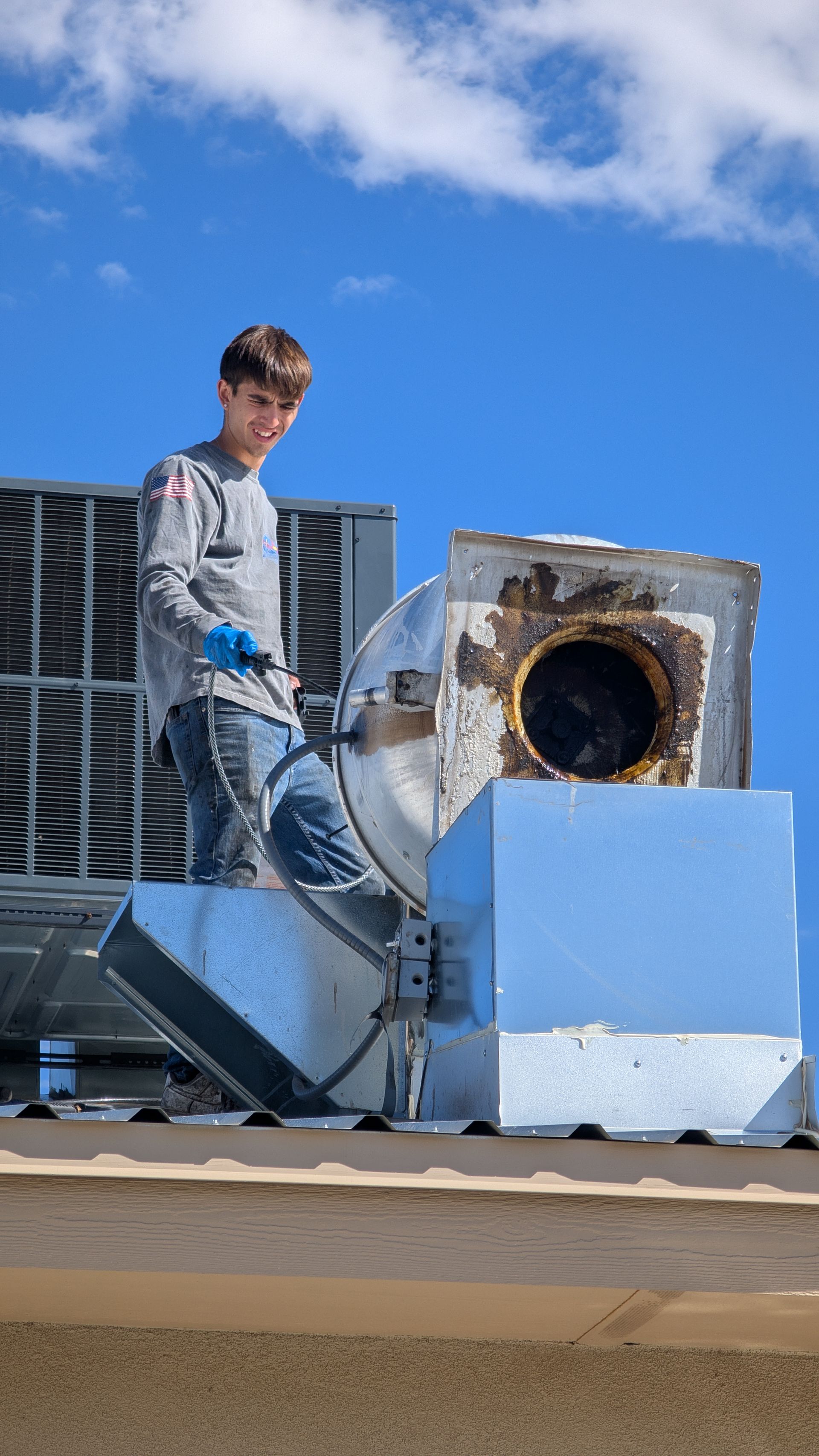 Man standing on a rooftop beside a large metal HVAC unit under a blue sky