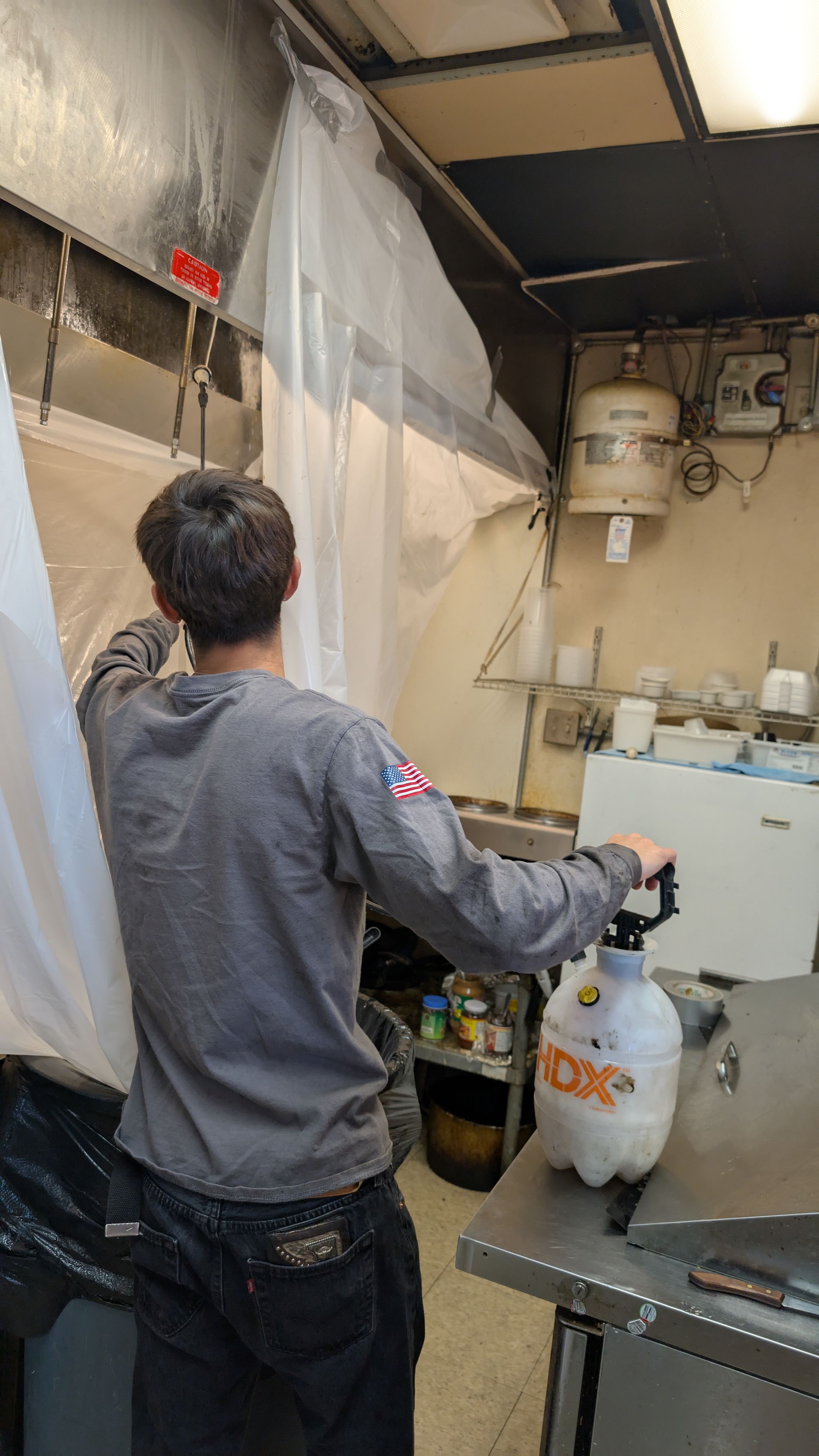 Person reaches toward a sink in a small kitchen, with a white bucket and hanging plastic curtain.