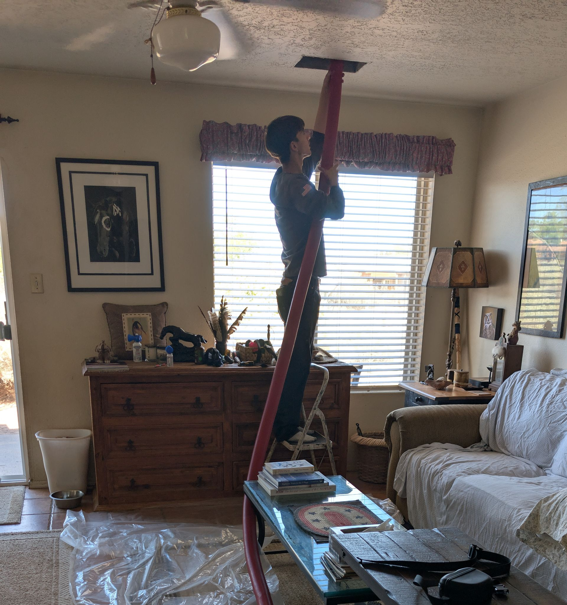 Person standing on a ladder, reaching up to install a ceiling light in a living room
