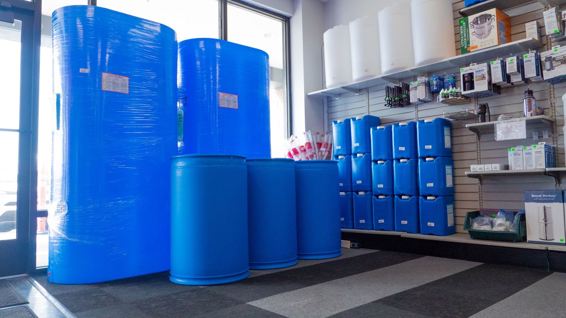 Blue plastic barrels and storage drums stacked in an industrial workspace near shelves and a window