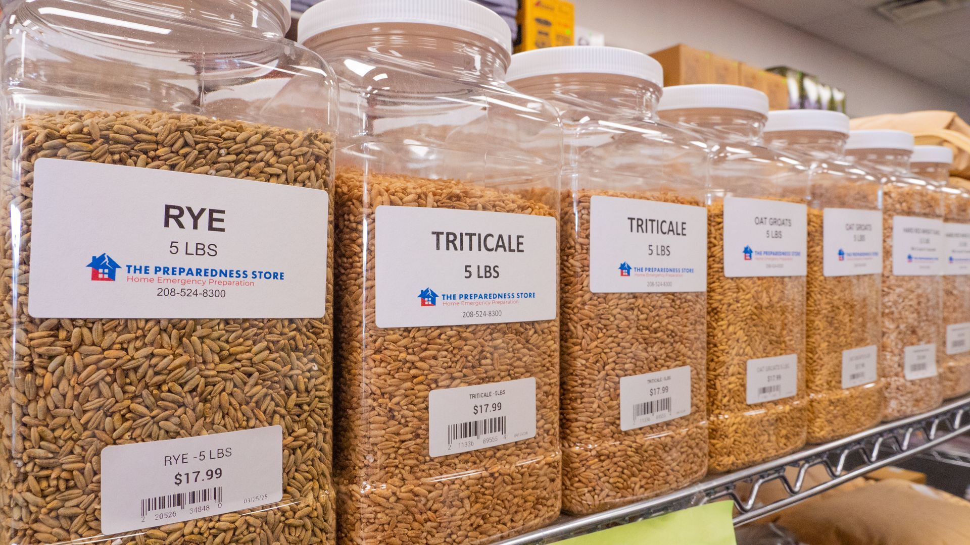 A shelf of clear plastic jars filled with grains like rye and triticale, labeled with prices, in a store.