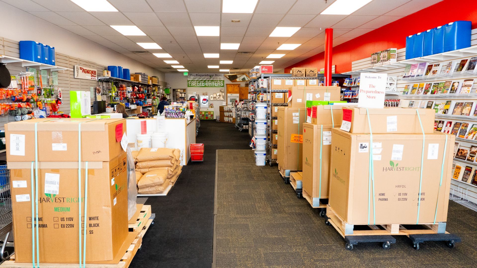 A store aisle with boxed merchandise on pallets and shelves stocked with various items.