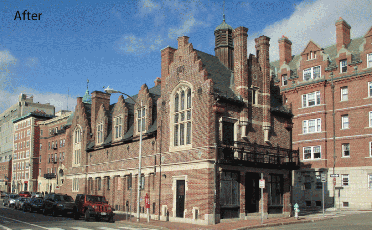 An angled exterior view of a historic brick building with stone trim, gabled roof, and chimney stacks on a sunny street.